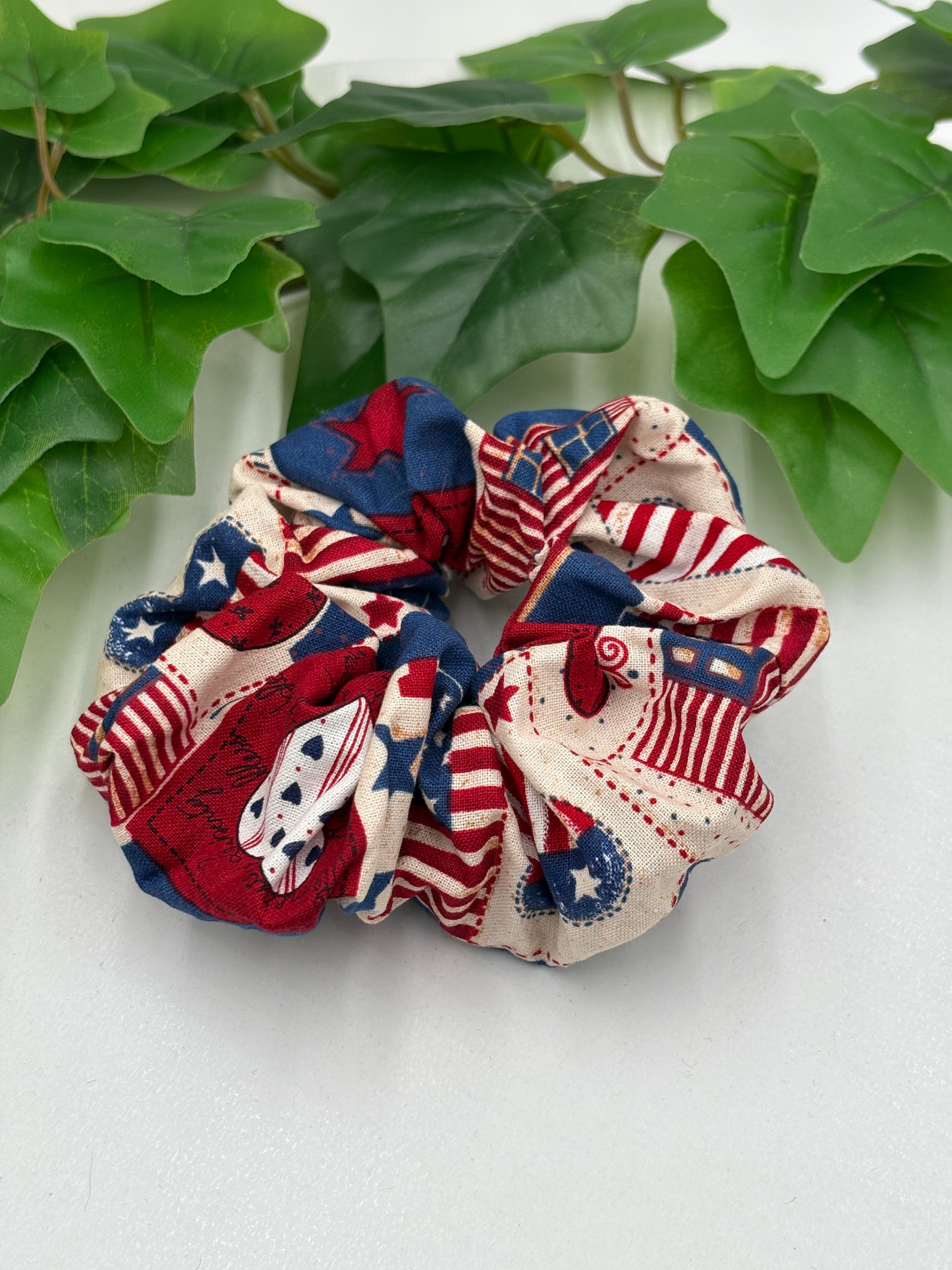 Red, white, and blue patterned scrunchie on a light background with green leaves.