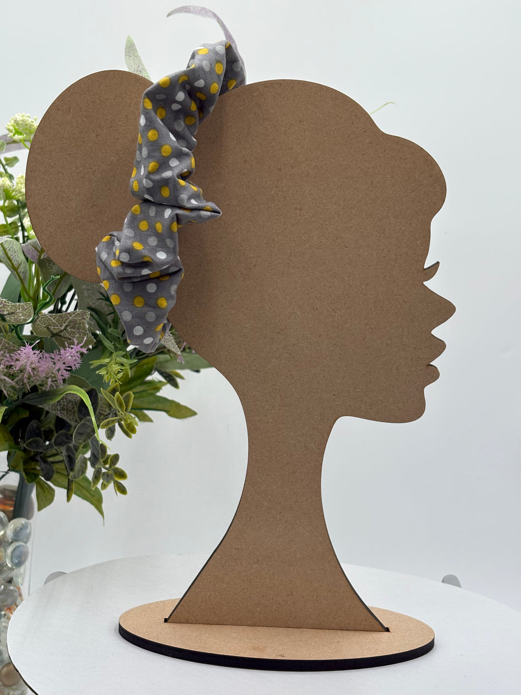 Gray with multicolored polka dots themed scrunchie on a mannequin head with a white background and greenery 