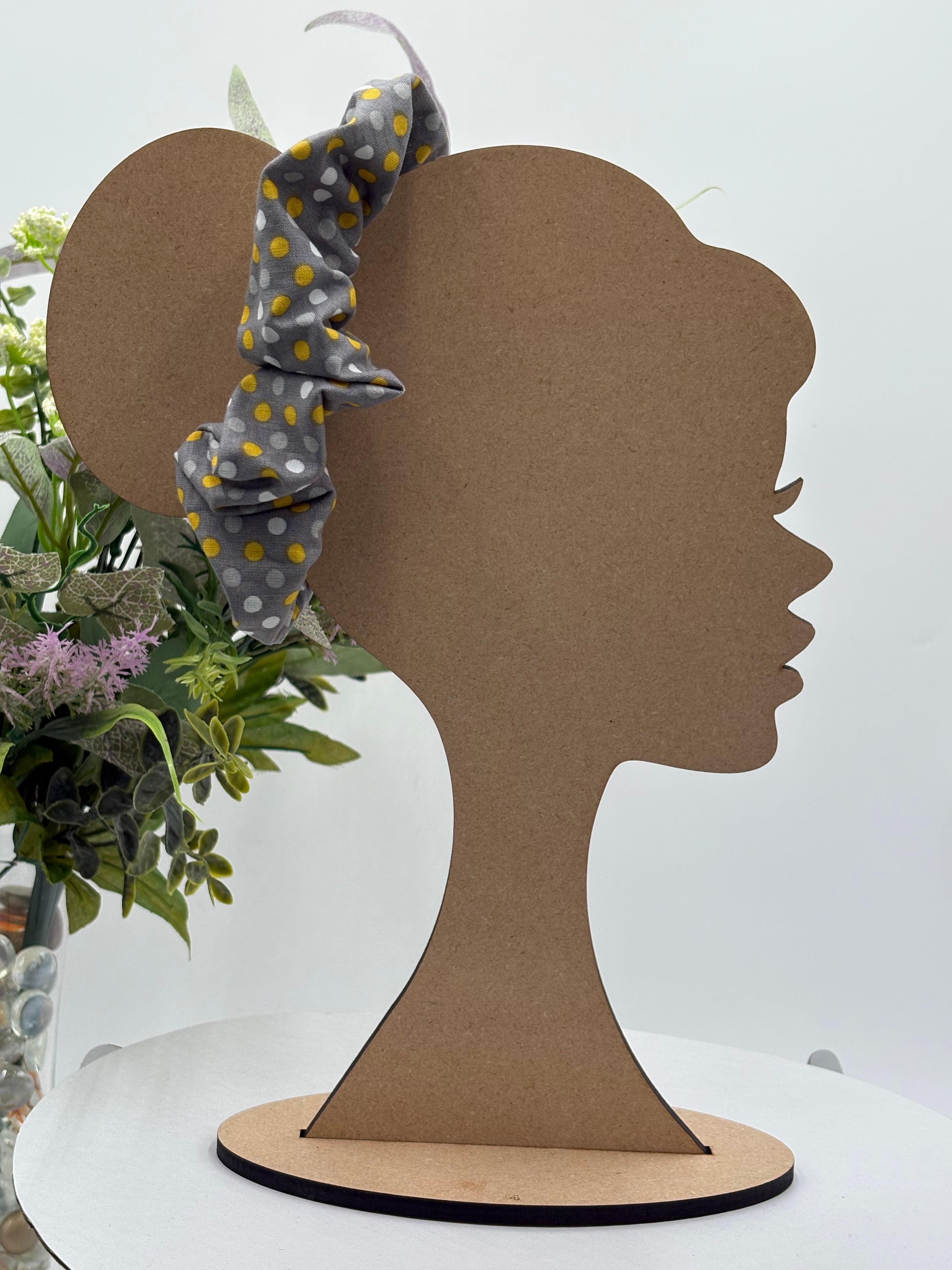 Gray with multicolored polka dots themed scrunchie on a mannequin head with a white background and greenery 