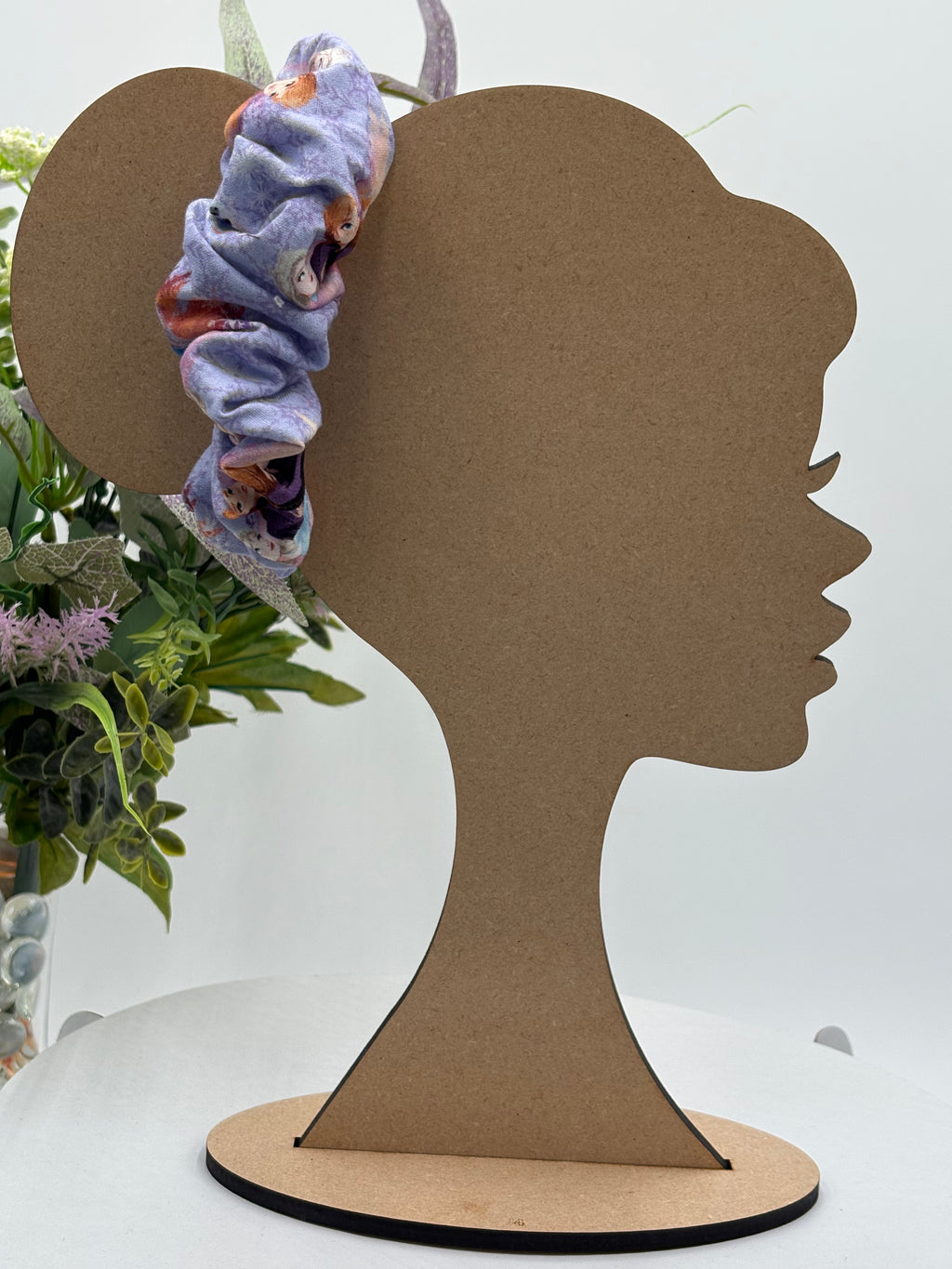 purple cartoon character themed scrunchie on a mannequin head with a white background and greenery 
