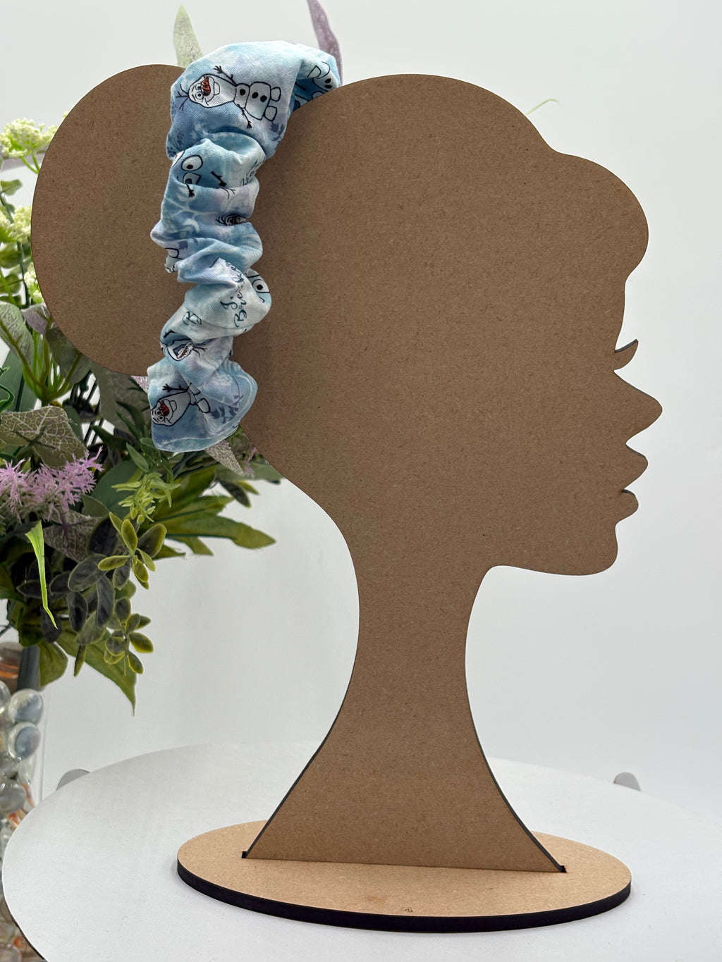 blue cartoon character themed scrunchie on a mannequin head with a white background and greenery 