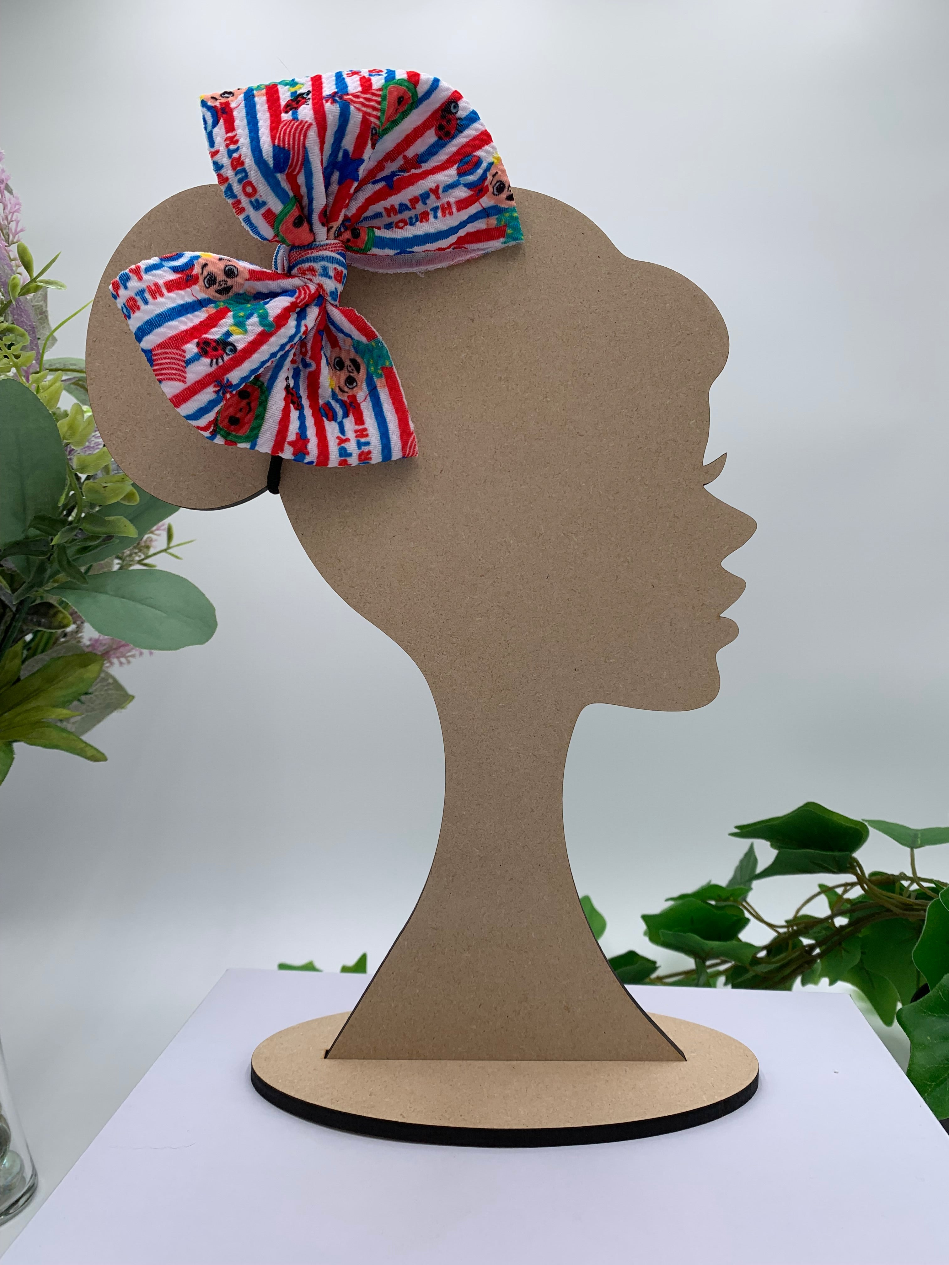 multicolored 4th of july themed hair bow on a wooden silhouette of a head with plants in the background