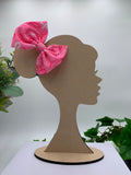 Pink hair bow on a wooden silhouette of a head with plants in the background