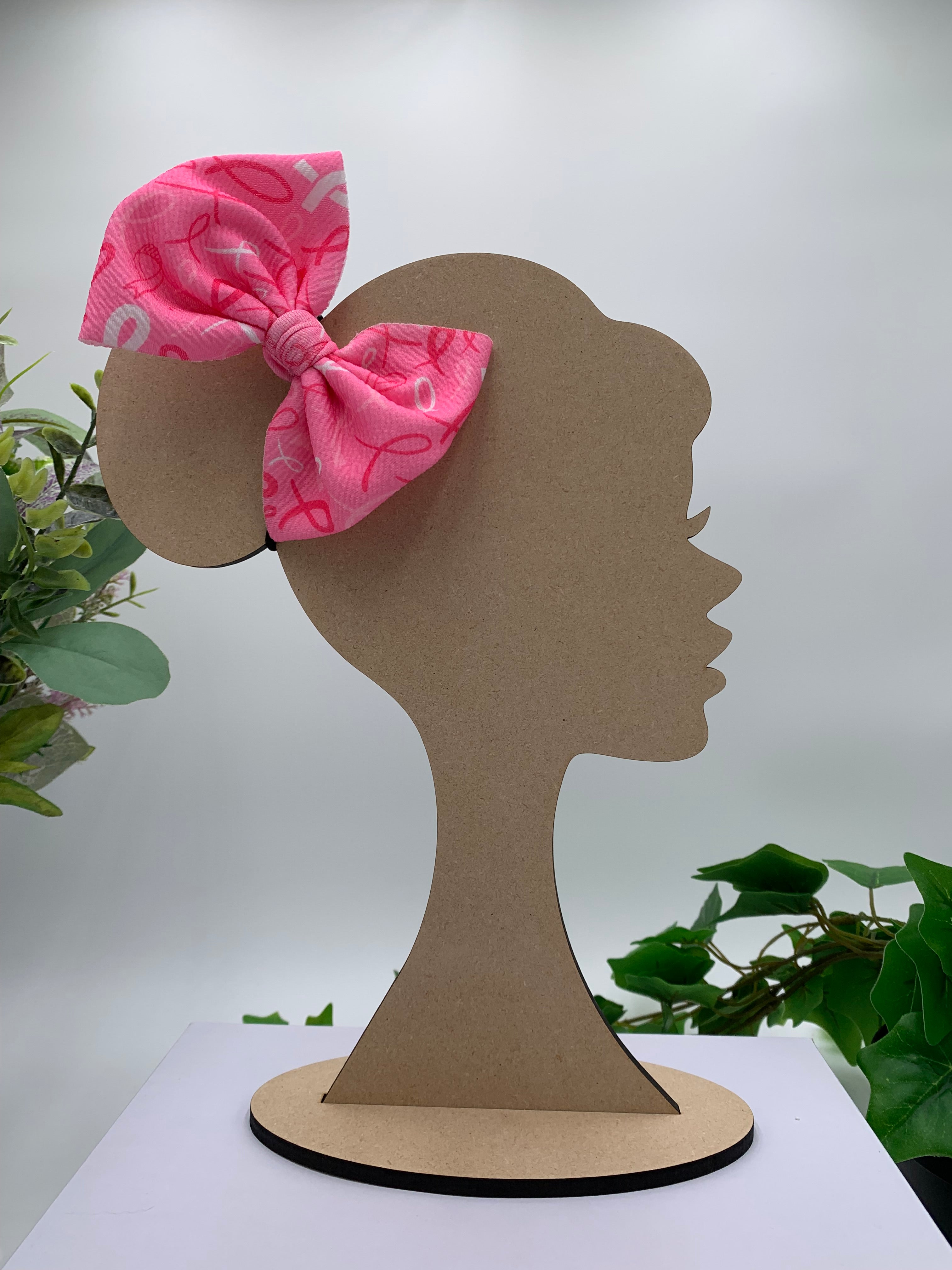 Pink hair bow on a wooden silhouette of a head with plants in the background