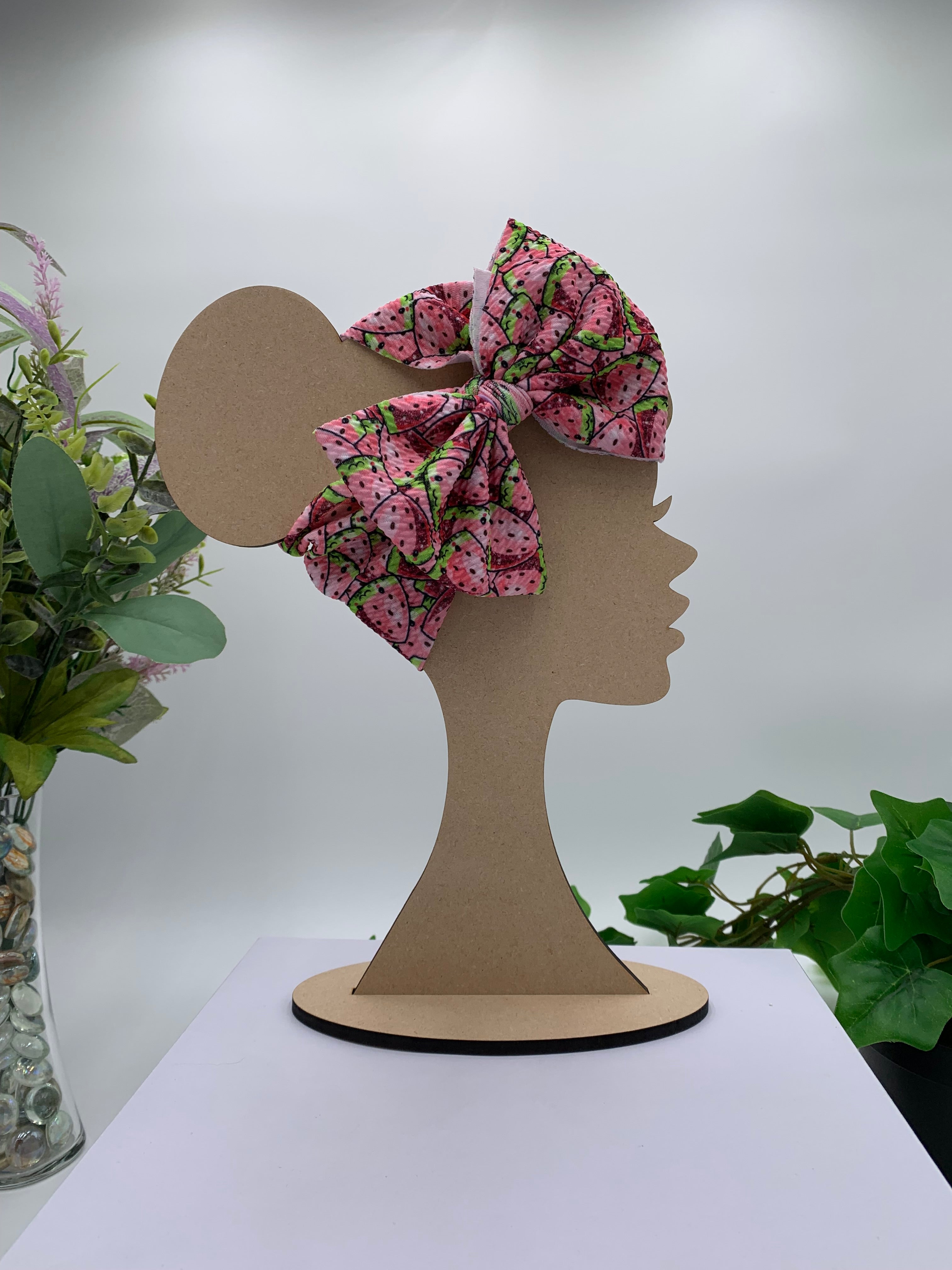 Watermelon slices themed big bow headband on a mannequin head with a white background and greenery 