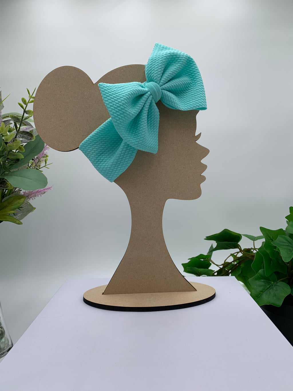 Celeste Blue big bow headband on a mannequin head with a white background and greenery 