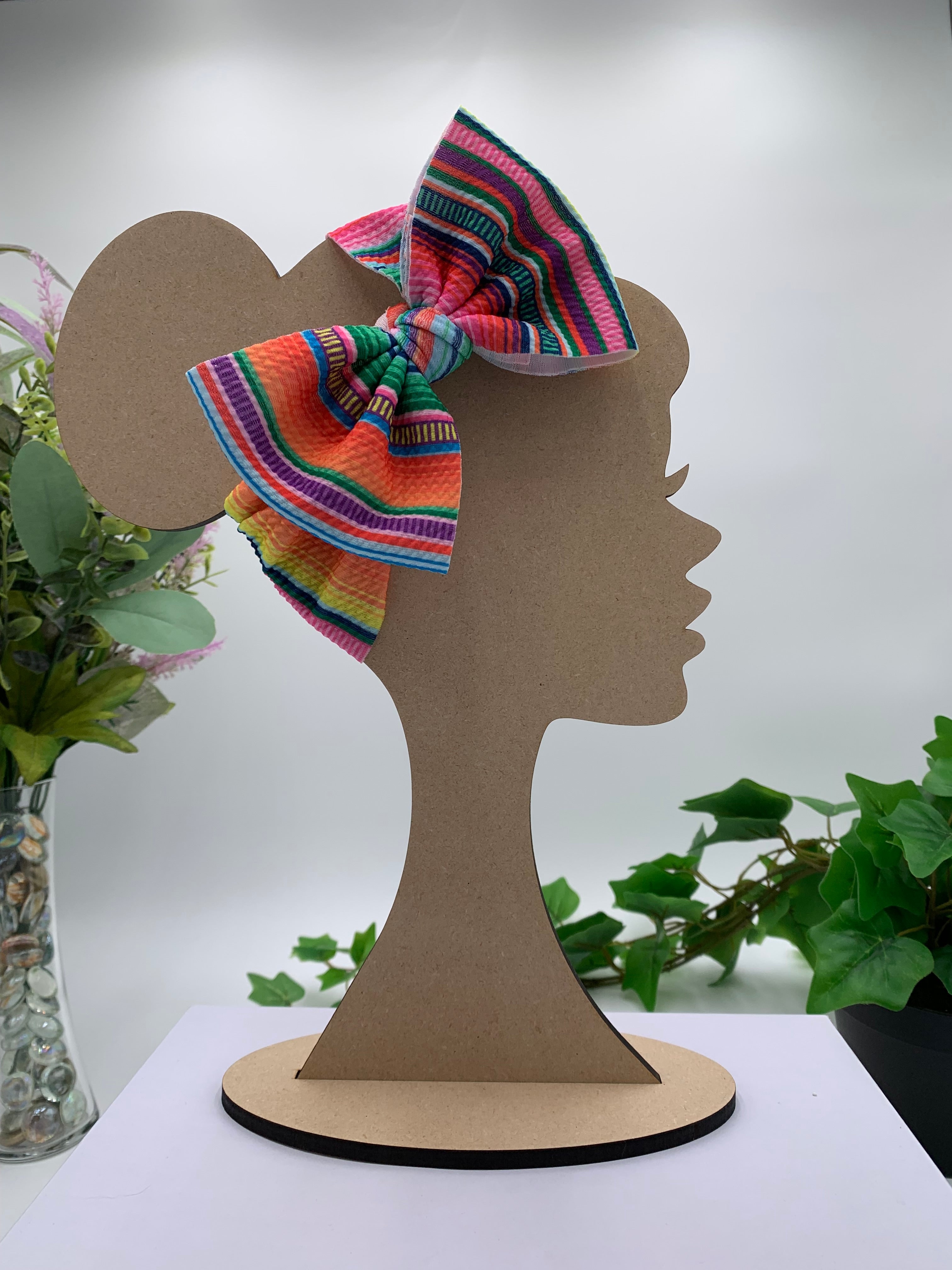 Colorful Serape themed big bow headband on a mannequin head with a white background and greenery 