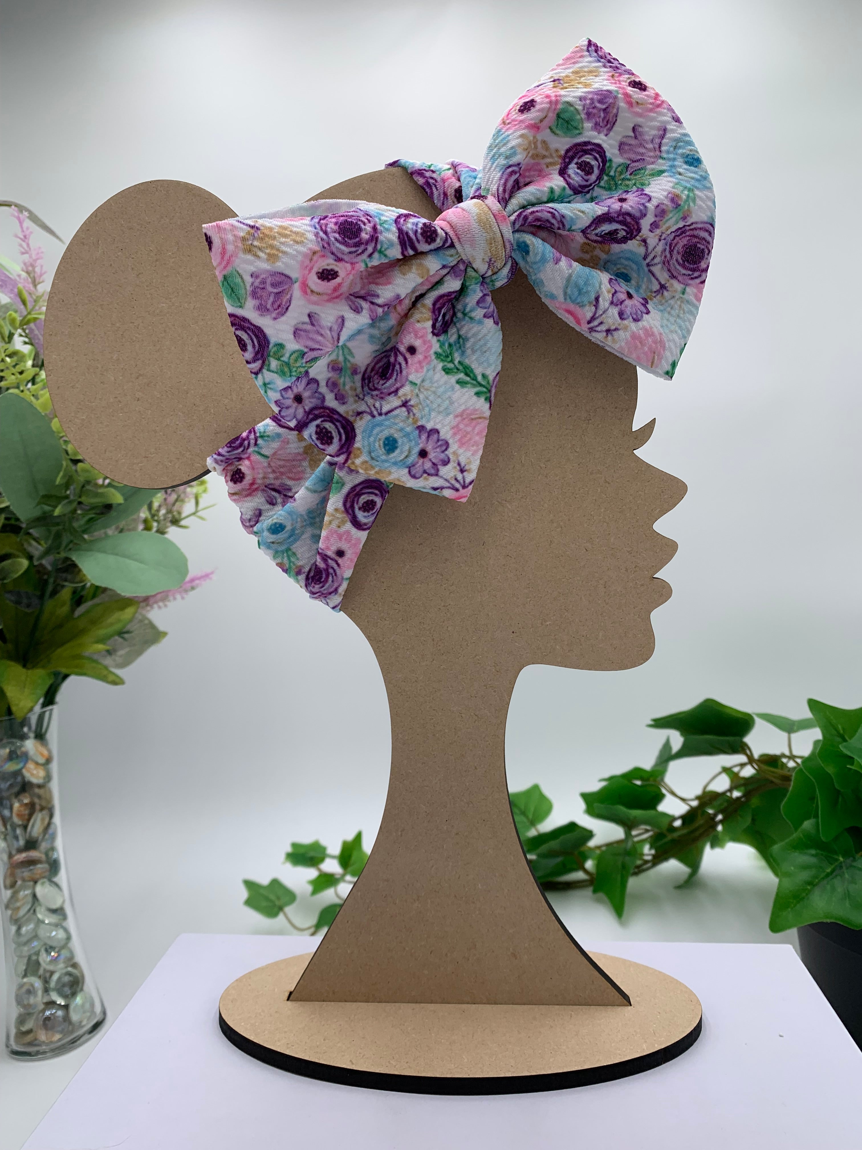 Spring flowers themed big bow headband on a mannequin head with a white background and greenery 