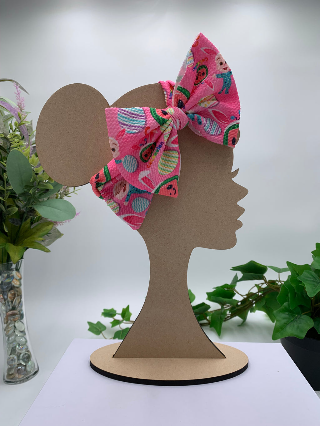 Hot Pink Easter themed big bow headband on a mannequin head with a white background and greenery 