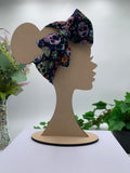 Day of the dead sugar skull themed big bow headband on a mannequin head with a white background and greenery 