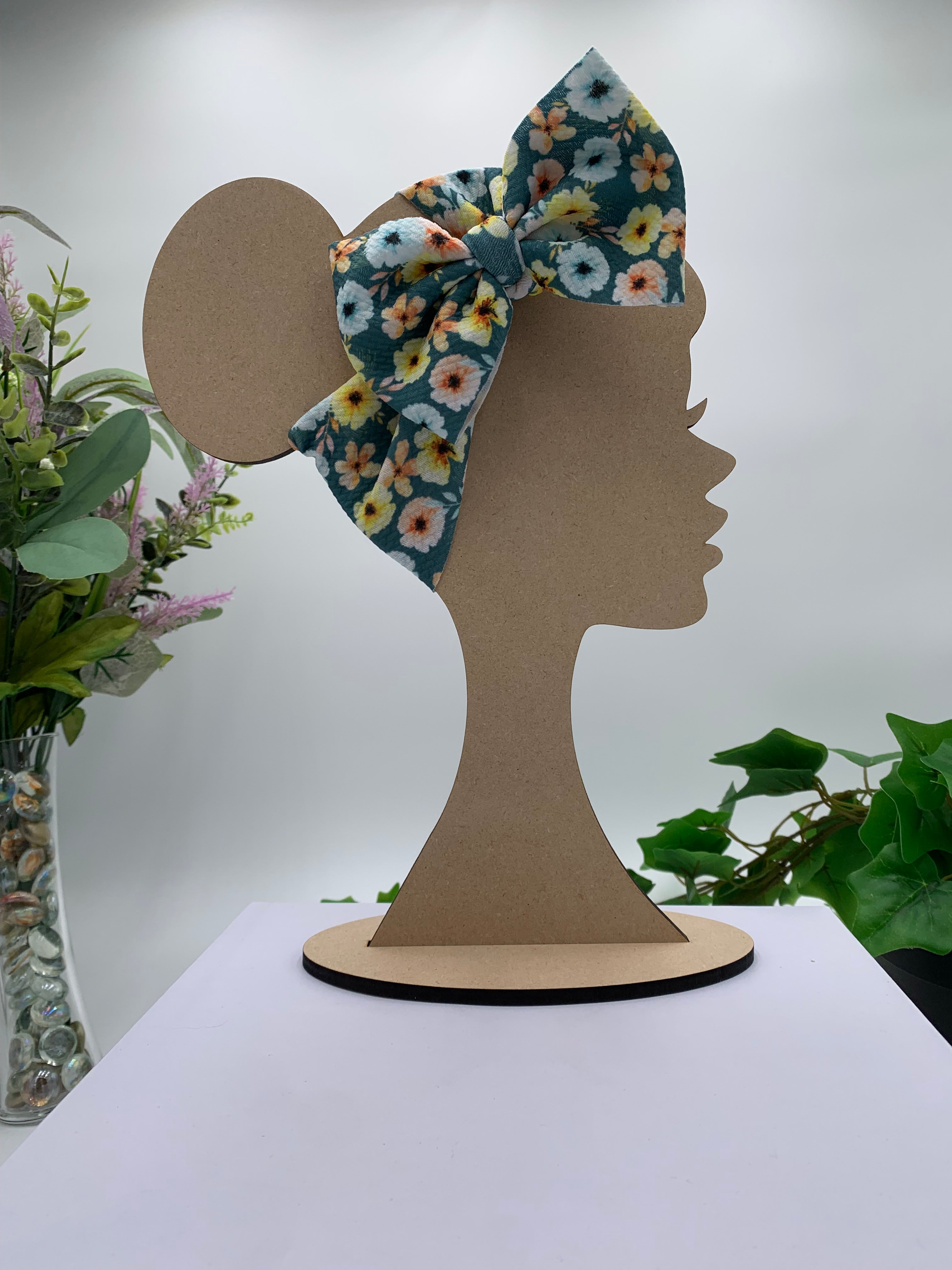 Colorful floral big bow headband on a mannequin head with a white background and greenery 
