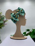 Green St. Patrick's Day themed big bow headband on a mannequin head with a white background and greenery 