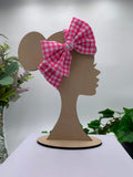 Pink plaid themed big bow headband on a mannequin head with a white background and greenery 