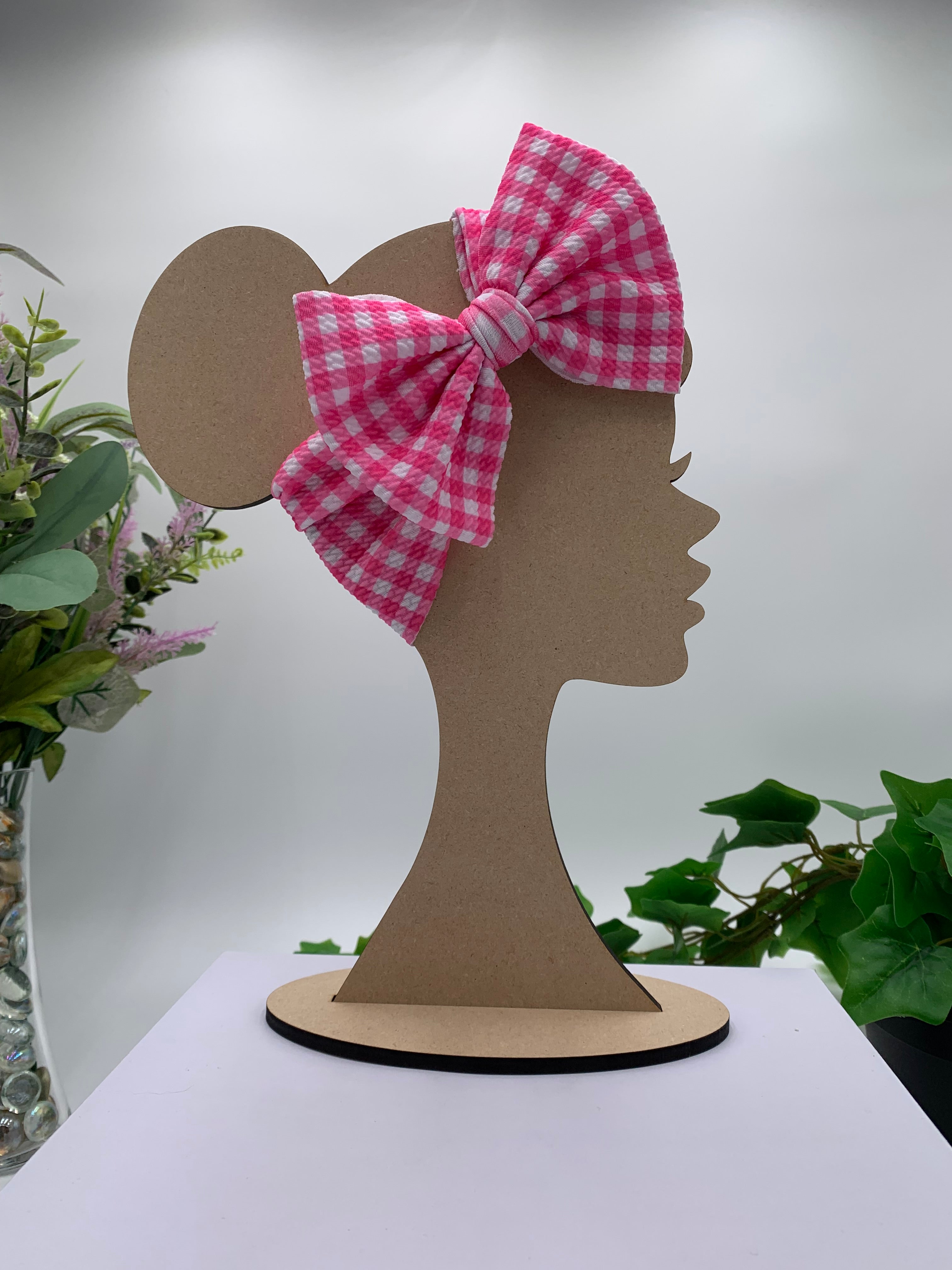 Pink plaid themed big bow headband on a mannequin head with a white background and greenery 