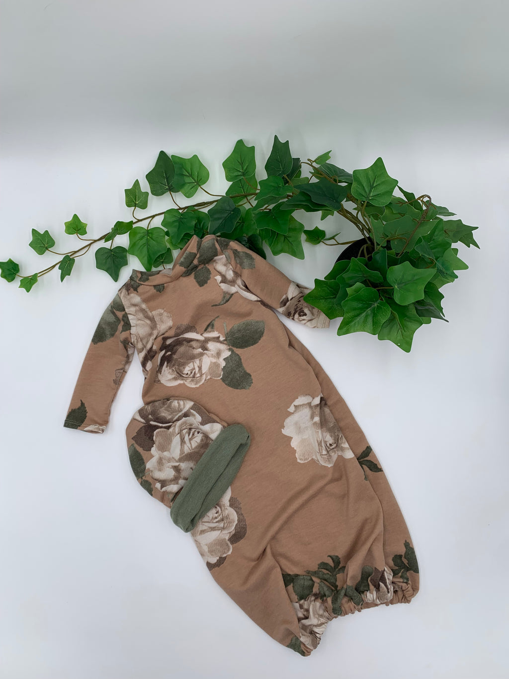 Floral baby sleeper sack with matching beanie on a white background with green leaves.