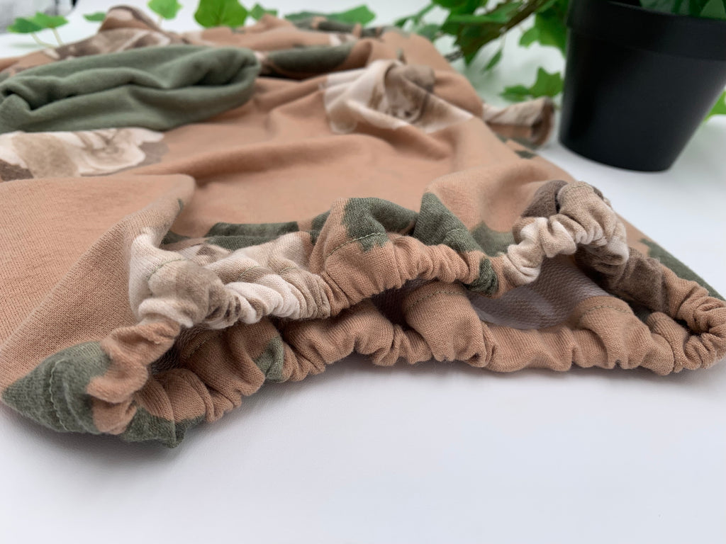 Close up of Floral baby sleeper sack with matching beanie on a white background with green leaves.