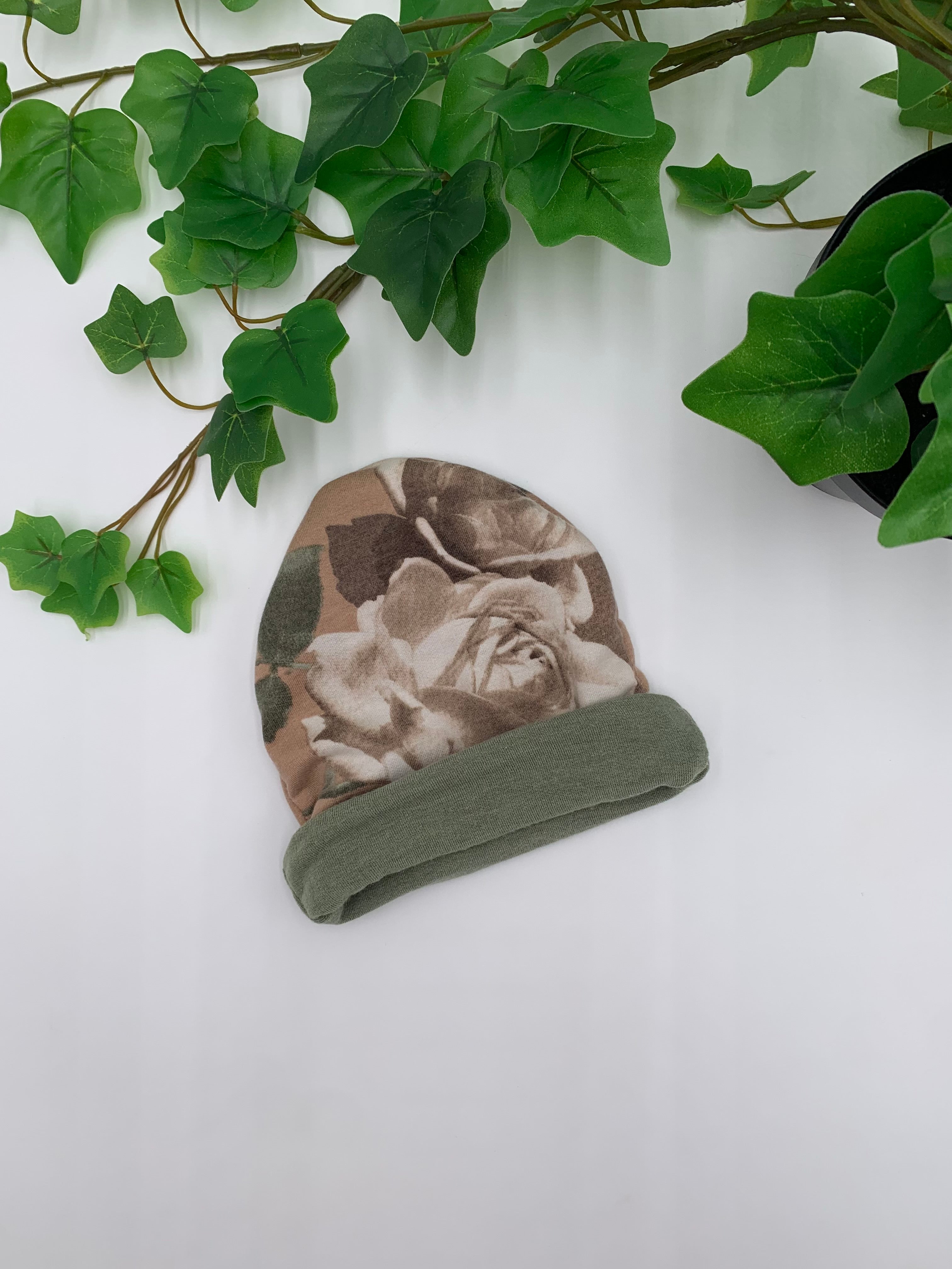 Baby beanie with floral pattern and green trim on a white background with green leaves.