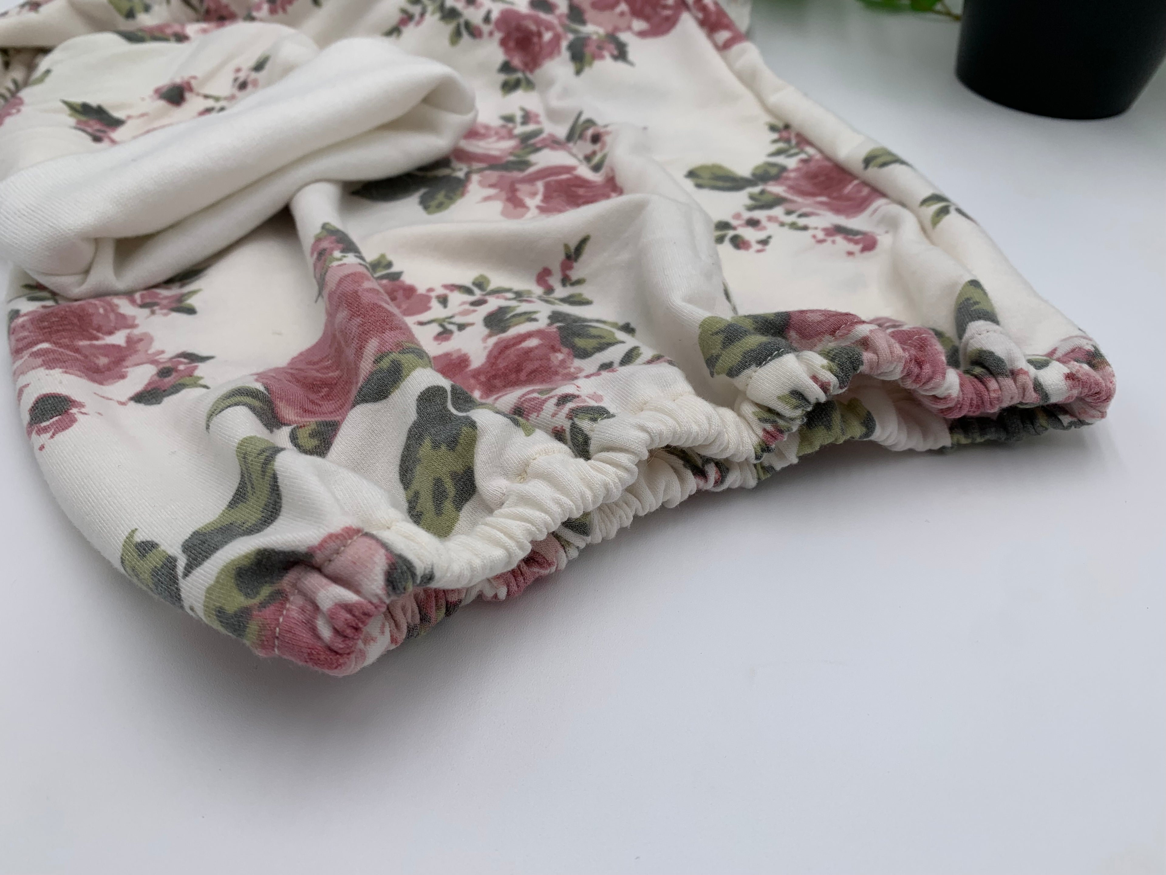 Close up of Floral baby sleeper sack with matching beanie on a white background with green leaves.