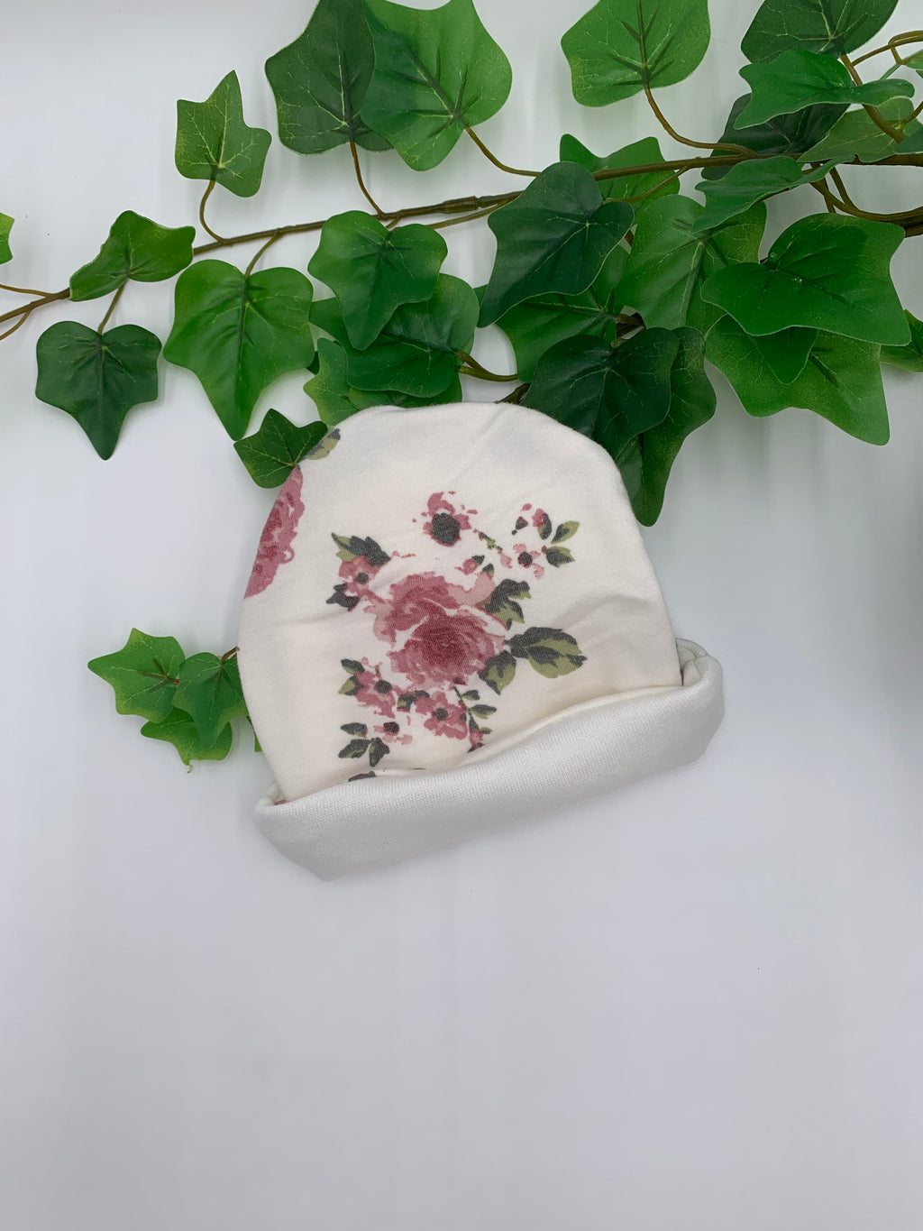 Floral-patterned fabric beanie on a white surface with green leaves