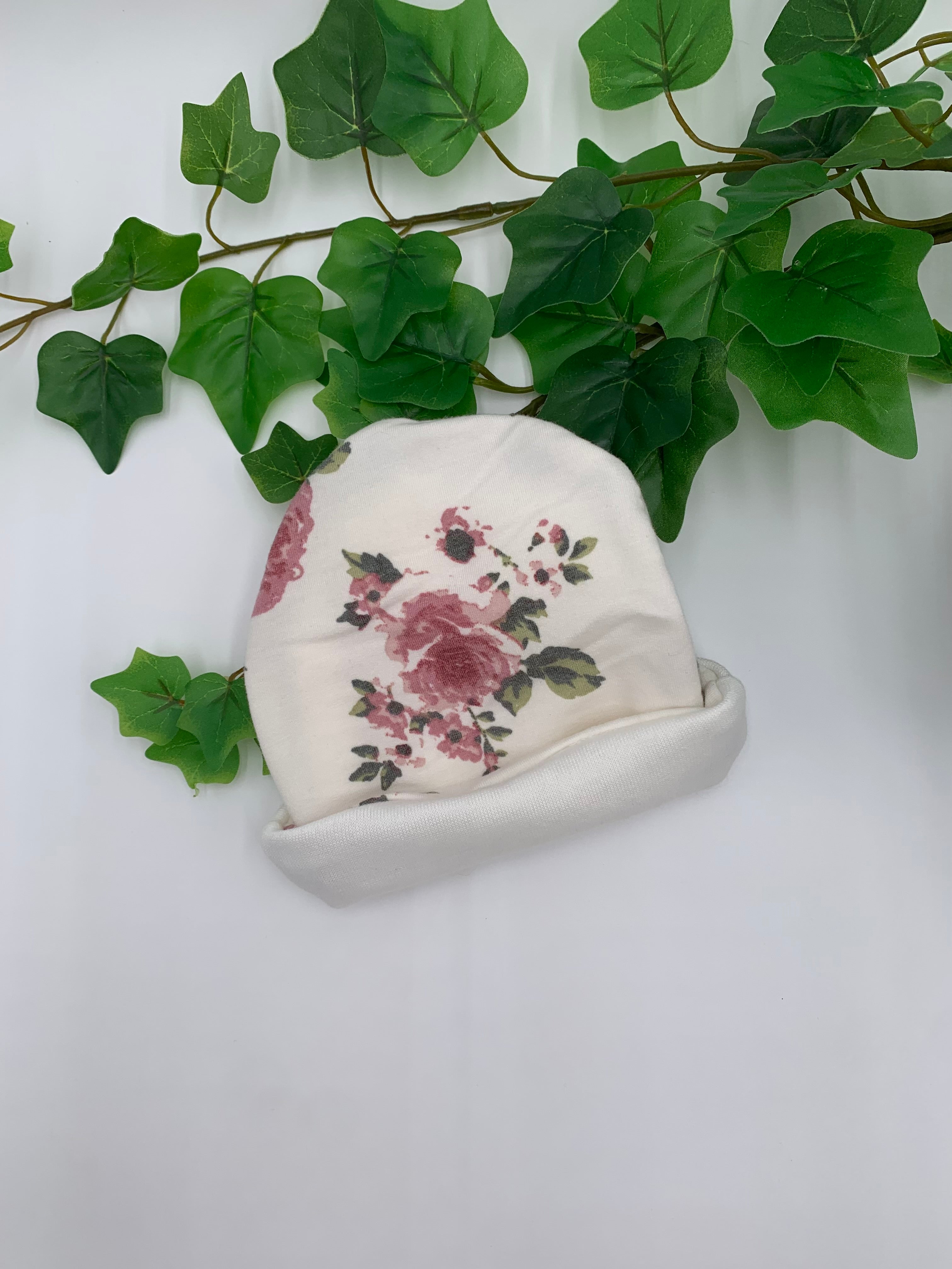 Floral-patterned fabric beanie on a white surface with green leaves