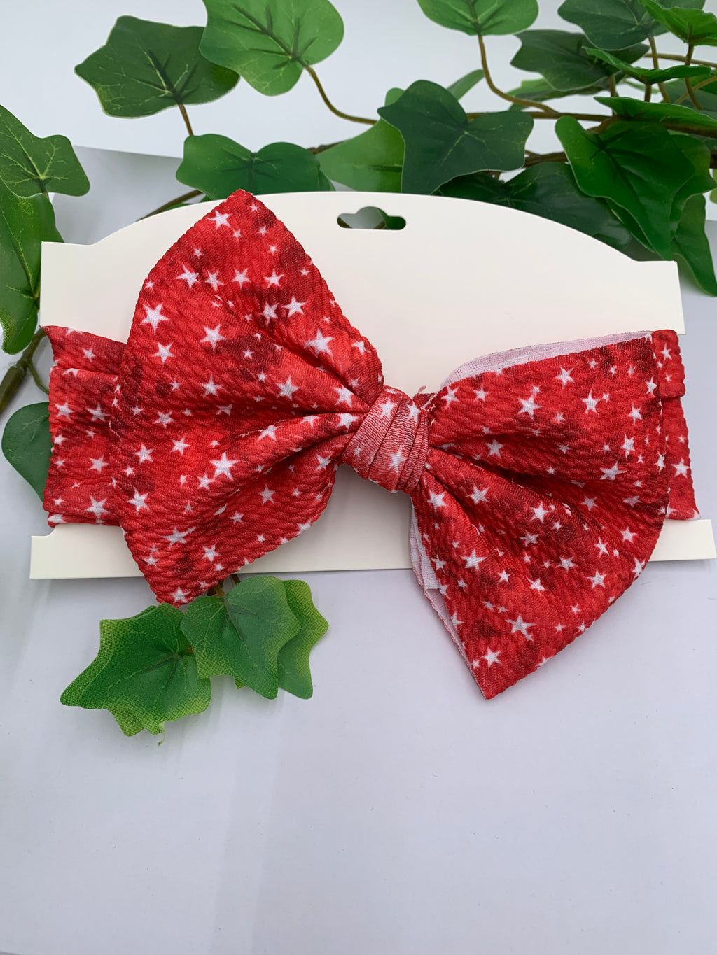 Red Start themed big bow headband on a white cardstock with a white background and greenery 
