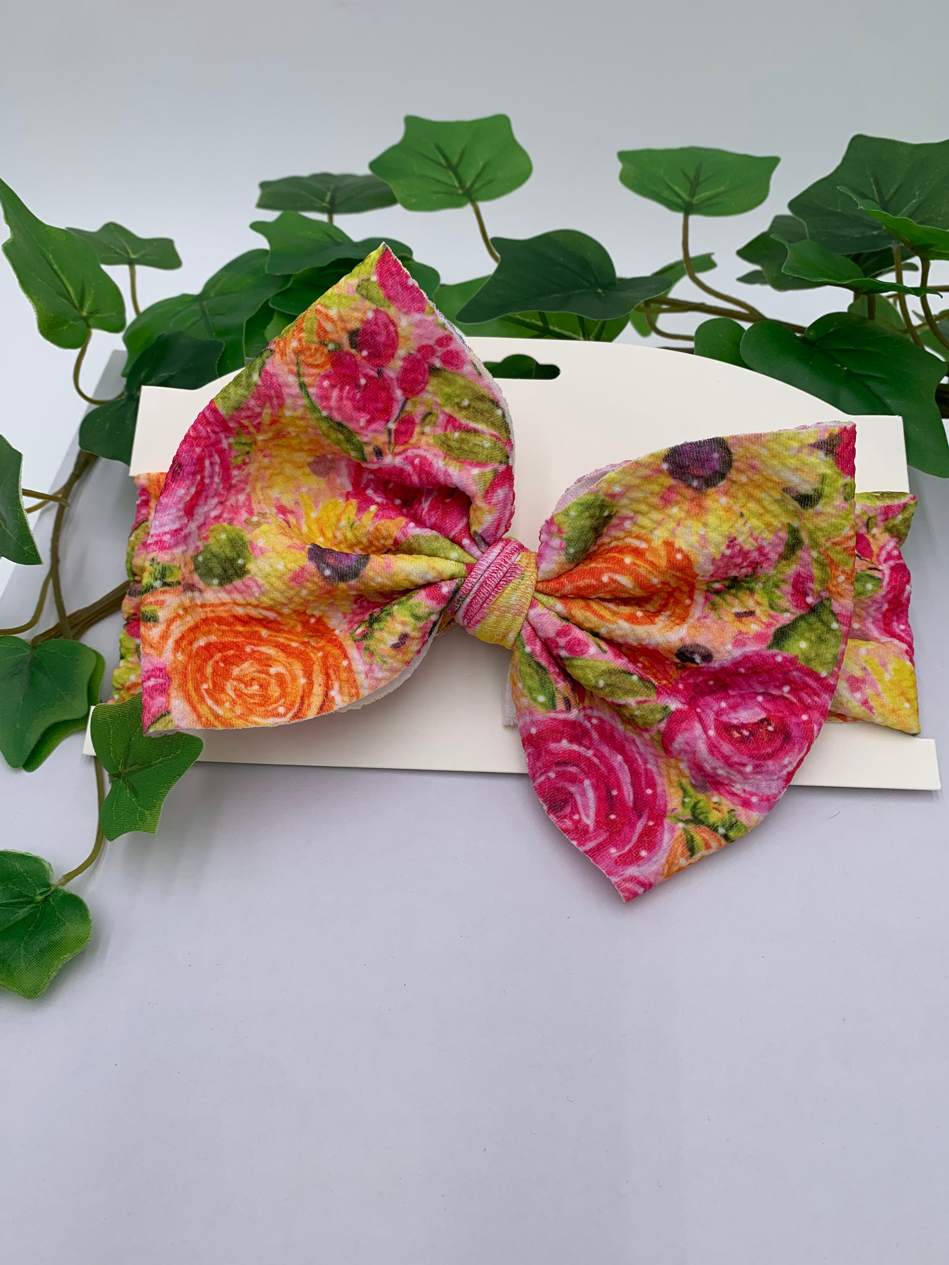 Spring flowers themed big bow headband on a white card stock with a white background and greenery 