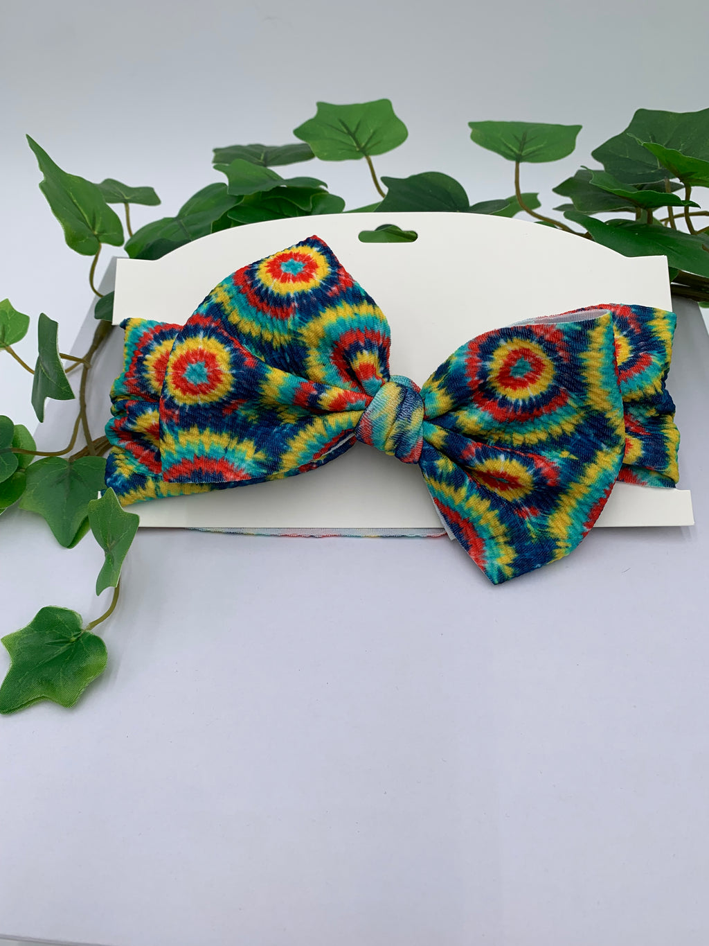 Colorful tie-dye bow on a white background with green leaves.