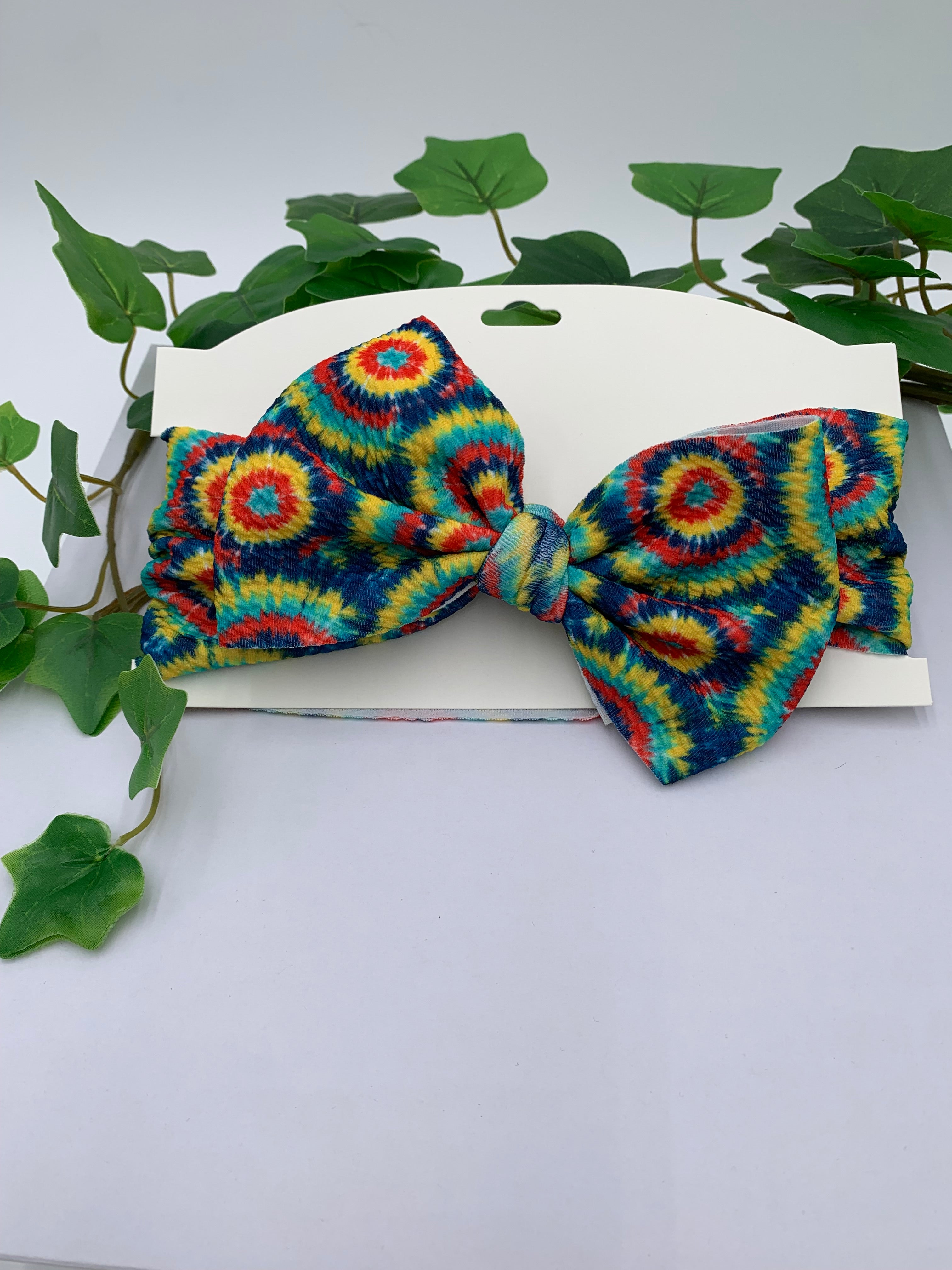 Colorful tie-dye bow on a white background with green leaves.