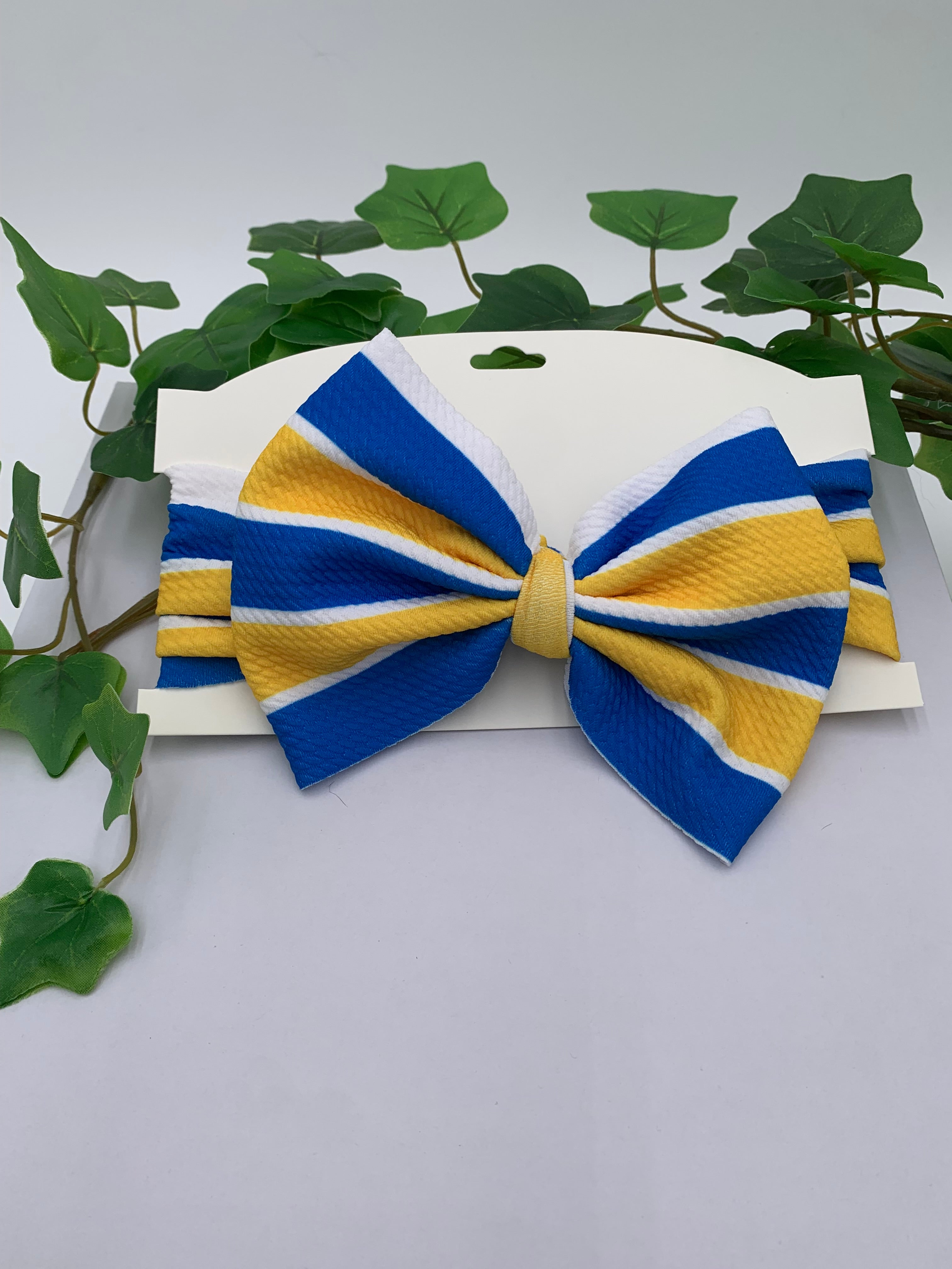 Blue and yellow striped big bow headband on a white background with green leaves.