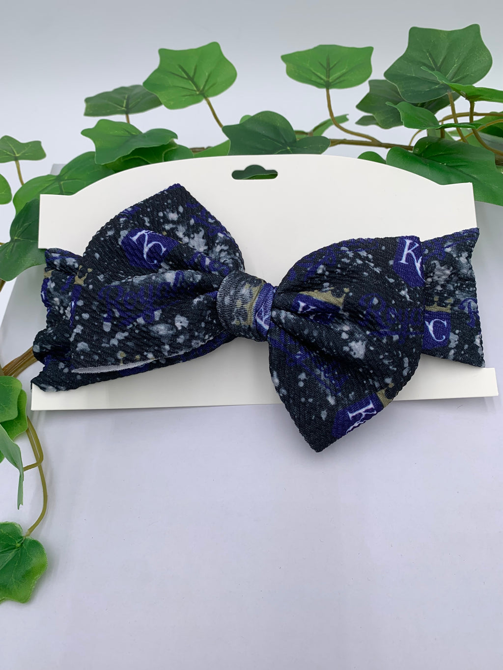 Navy blue big bow headband with white patterns on a white card with green leaves in the background