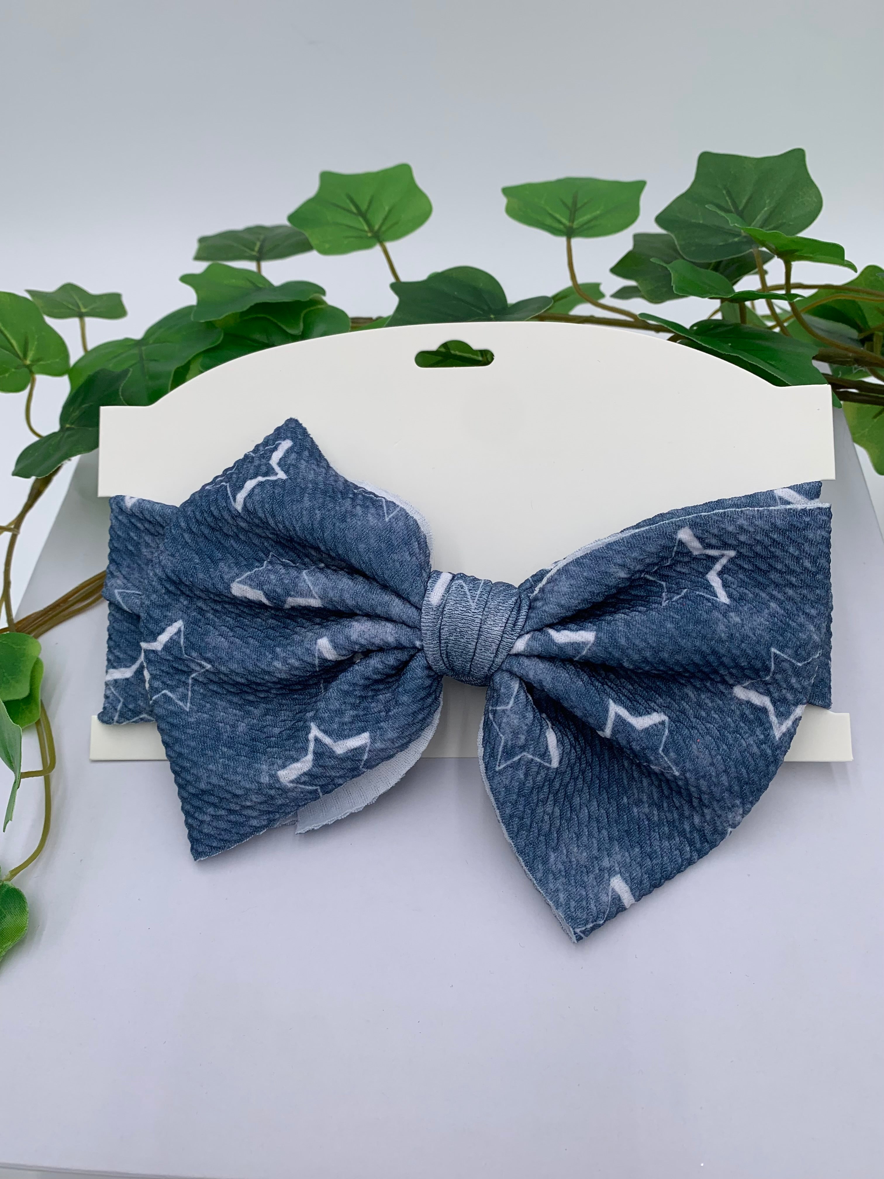 Blue with White starts themed big bow headband on a white card with a white background and greenery 
