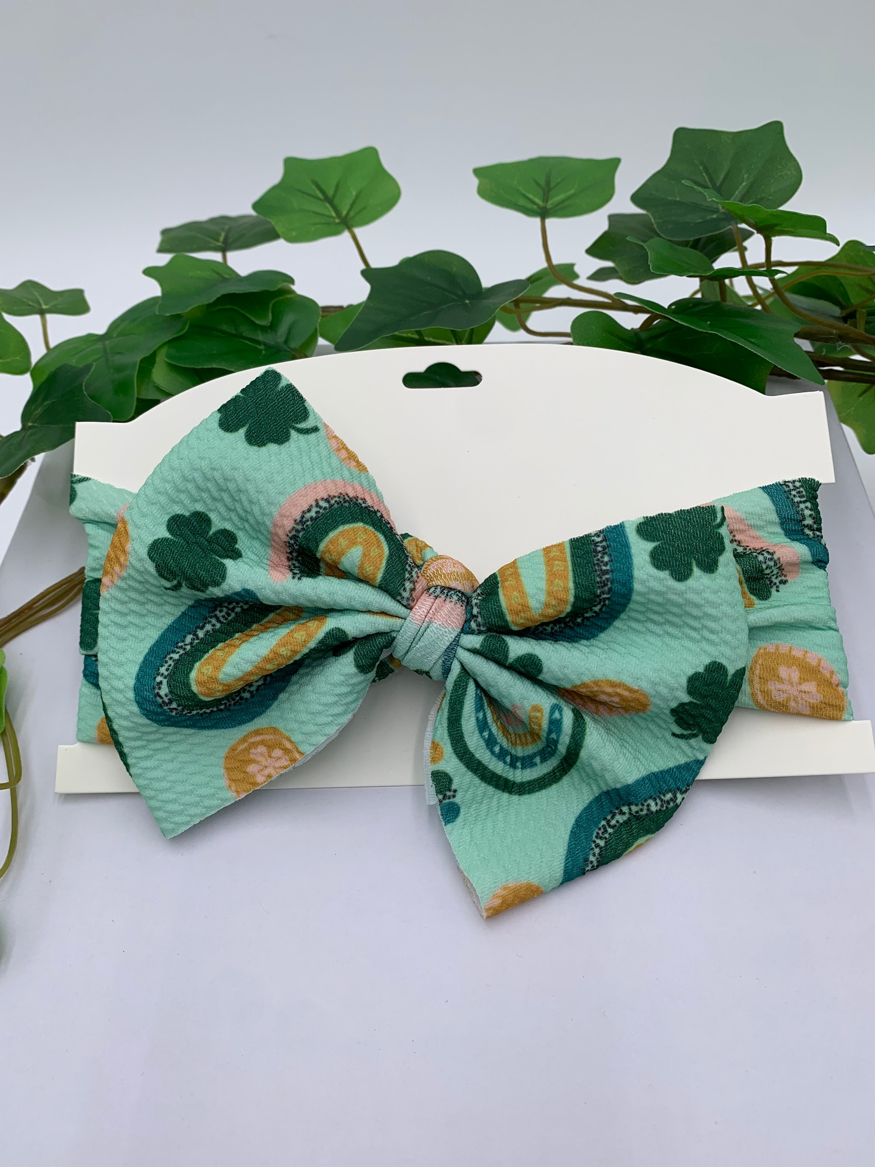 Green St. Patrick's Day themed big bow headband on a white card with a white background and greenery 