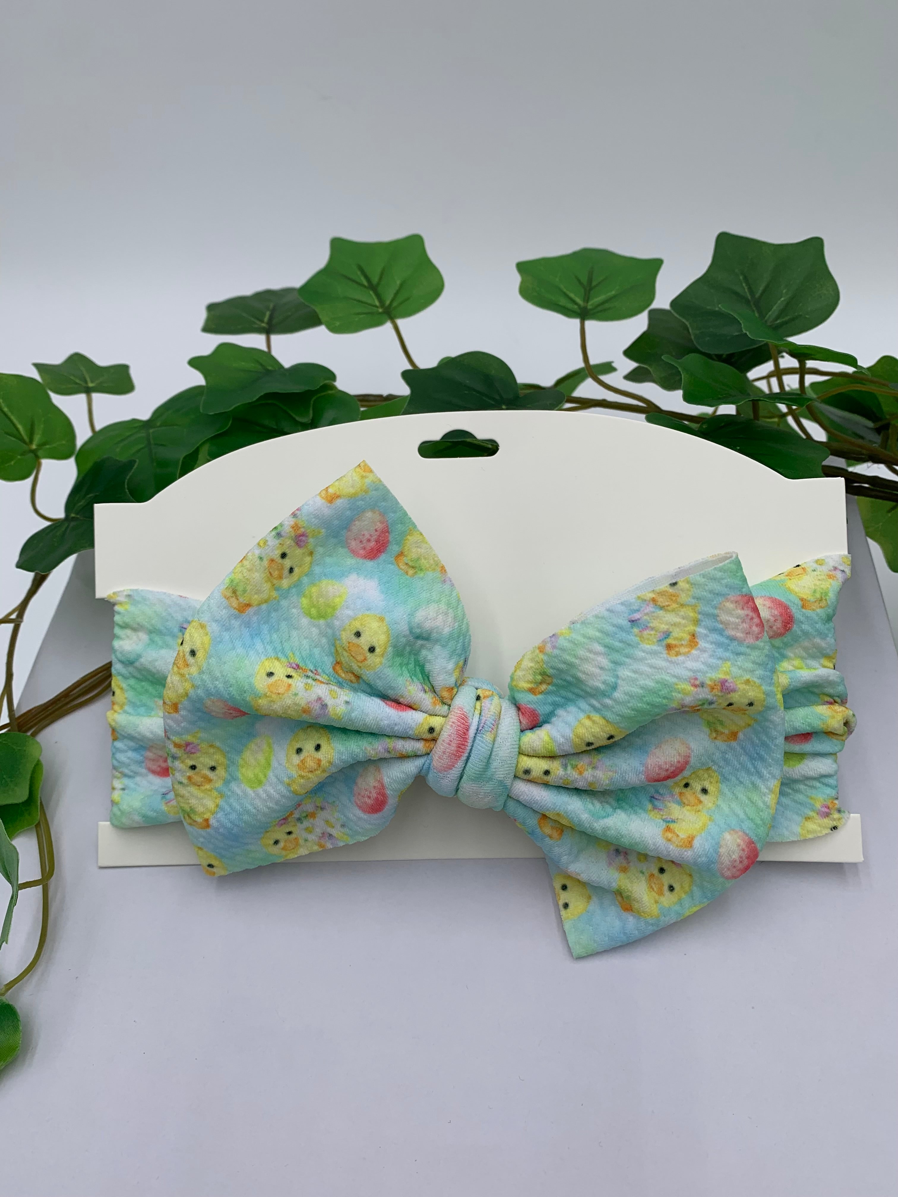 Rubber Duck themed big bow headband on a white card with a white background and greenery 