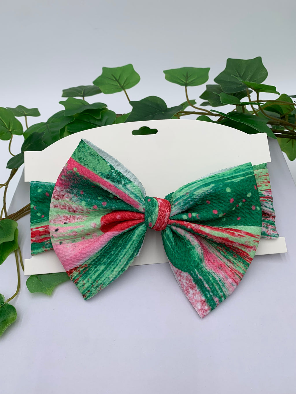 Watermelon colors themed big bow headband on a white card with a white background and greenery 