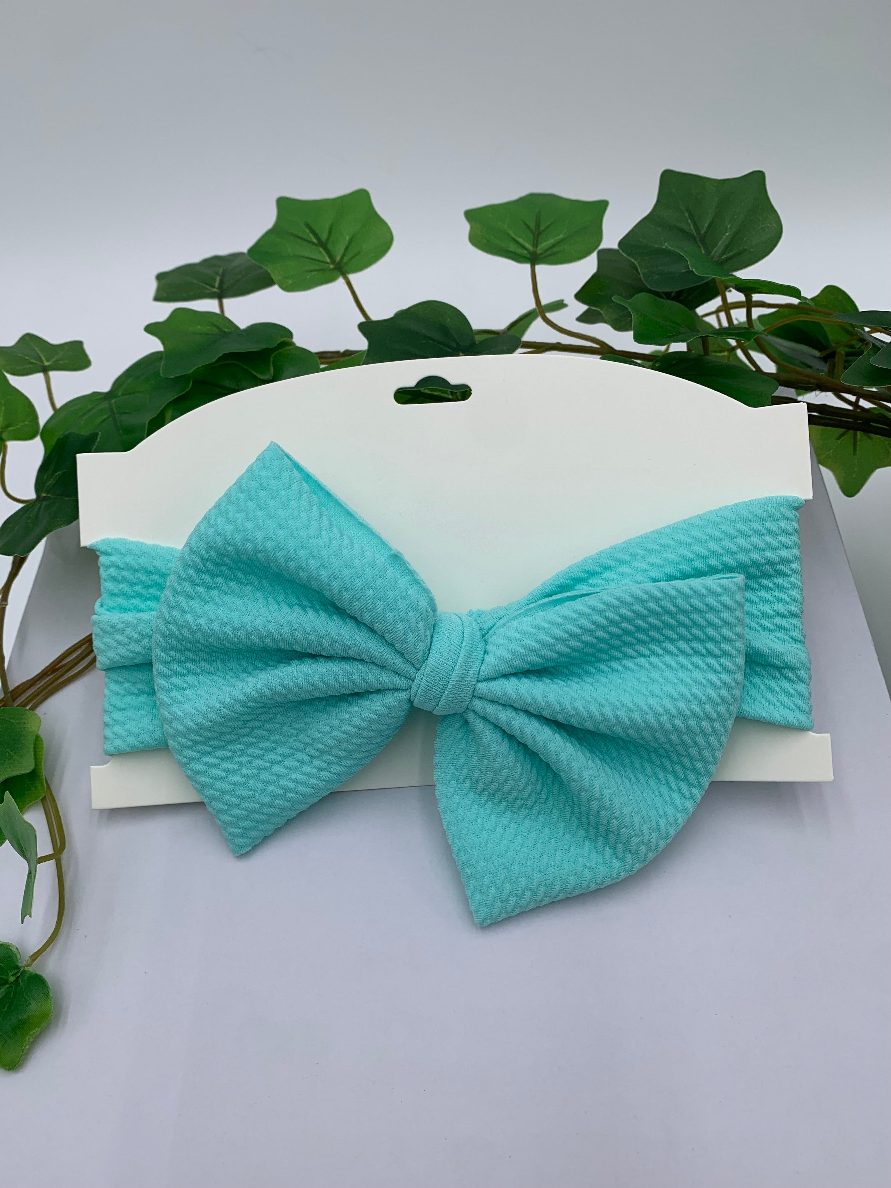 Celeste blue big bow headband on a white card with a white background and greenery 