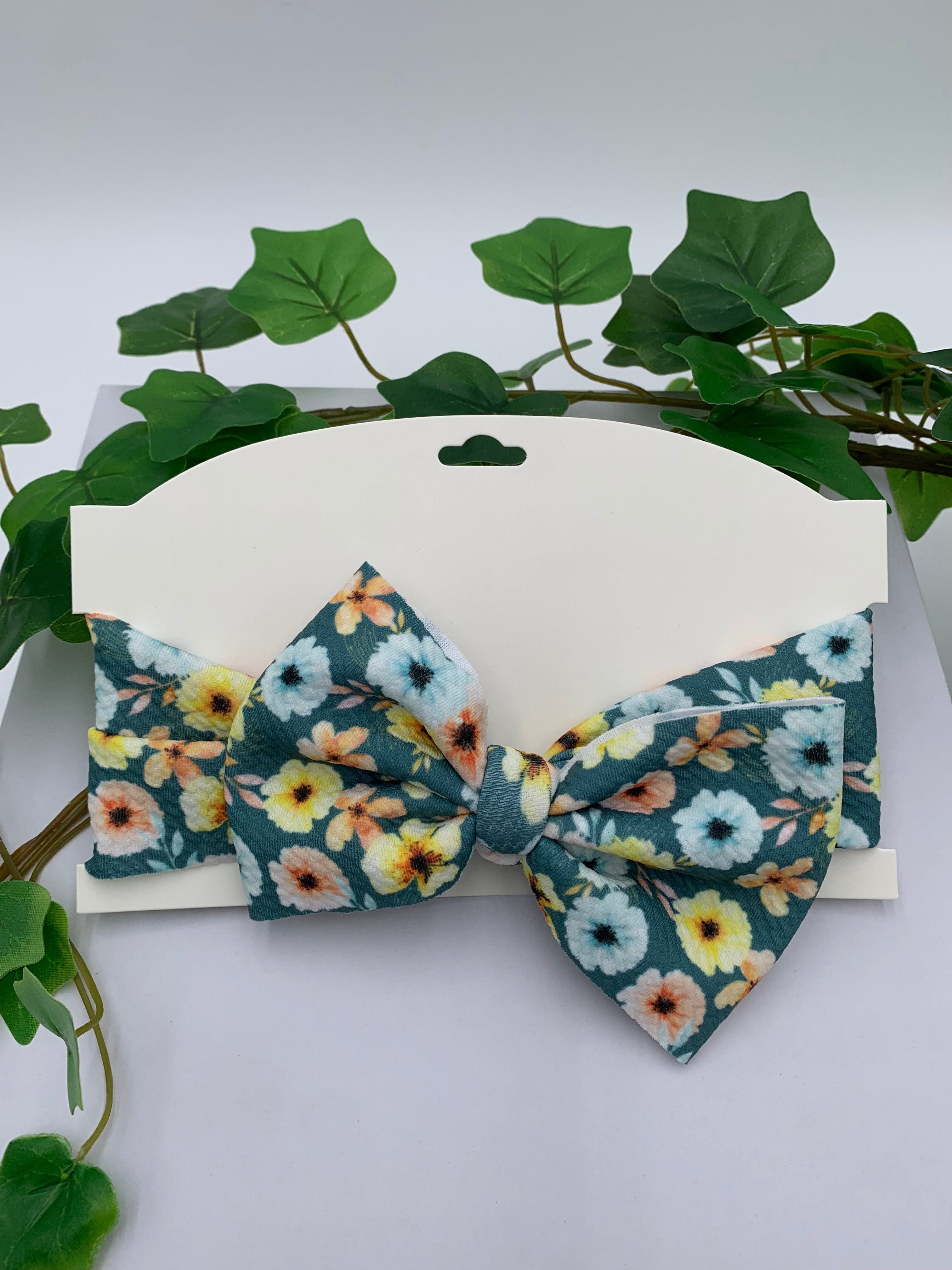 Floral-patterned big bow headband on a white card with green leaves in the background