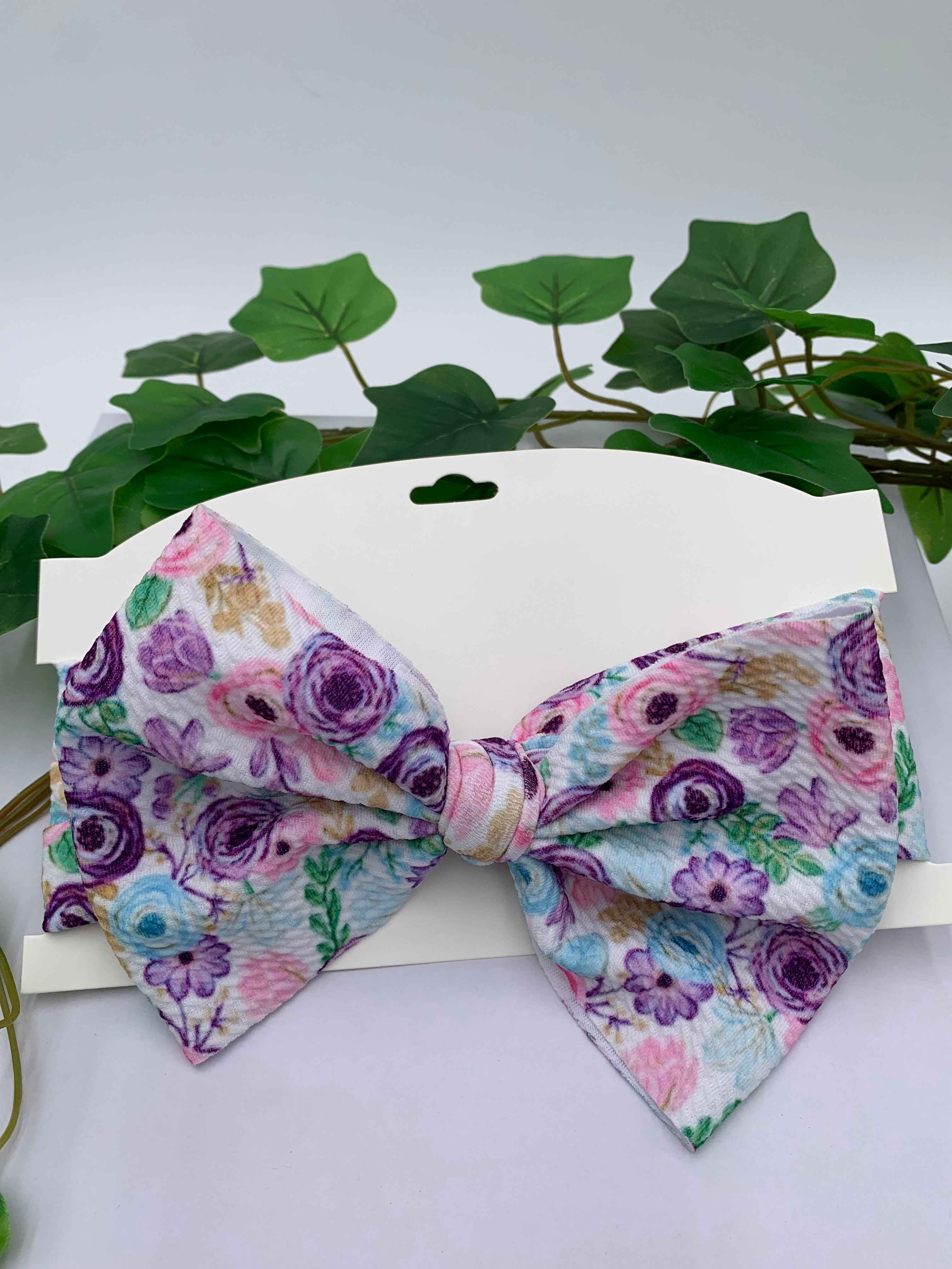 Spring flowers themed big bow headband on a white cardstock with a white background and greenery 