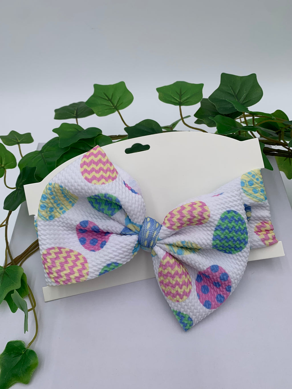 Easter eggs themed big bow headband on a white card with a white background and greenery 