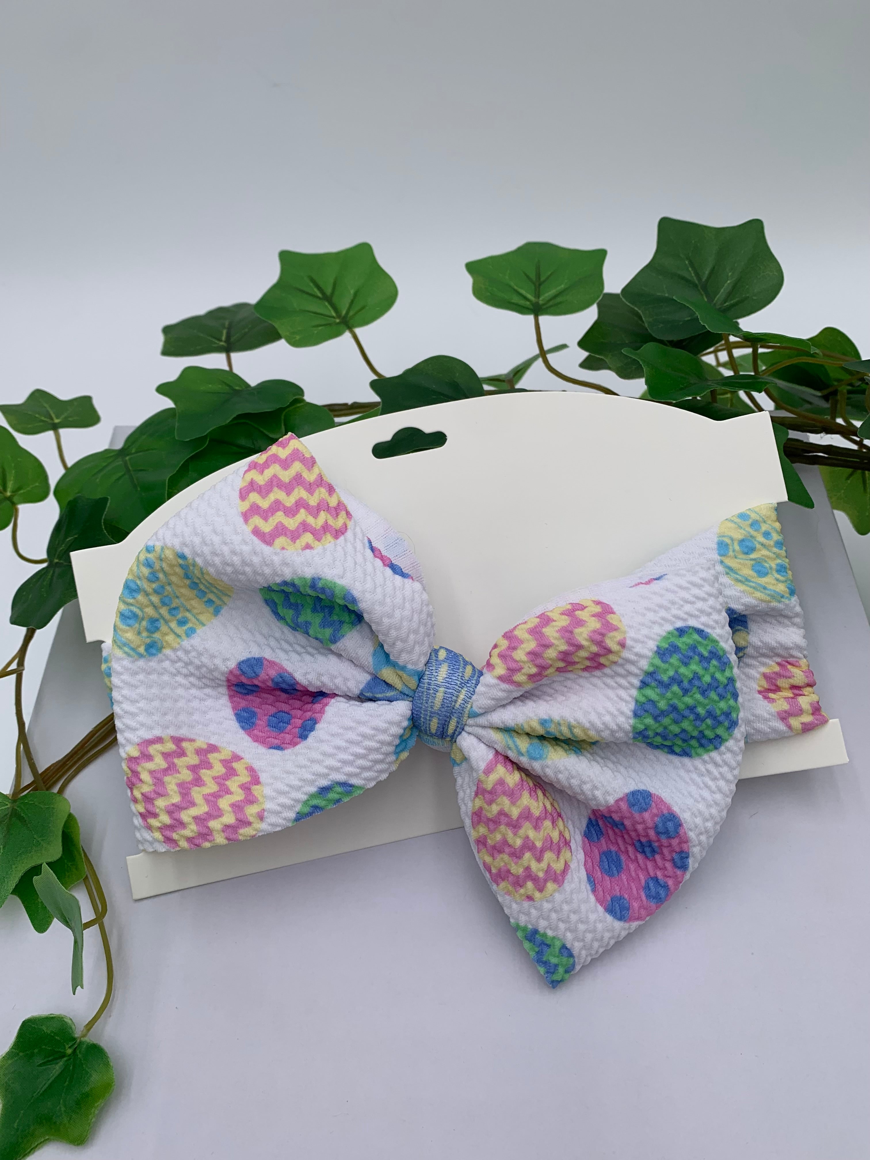 Easter eggs themed big bow headband on a white card with a white background and greenery 