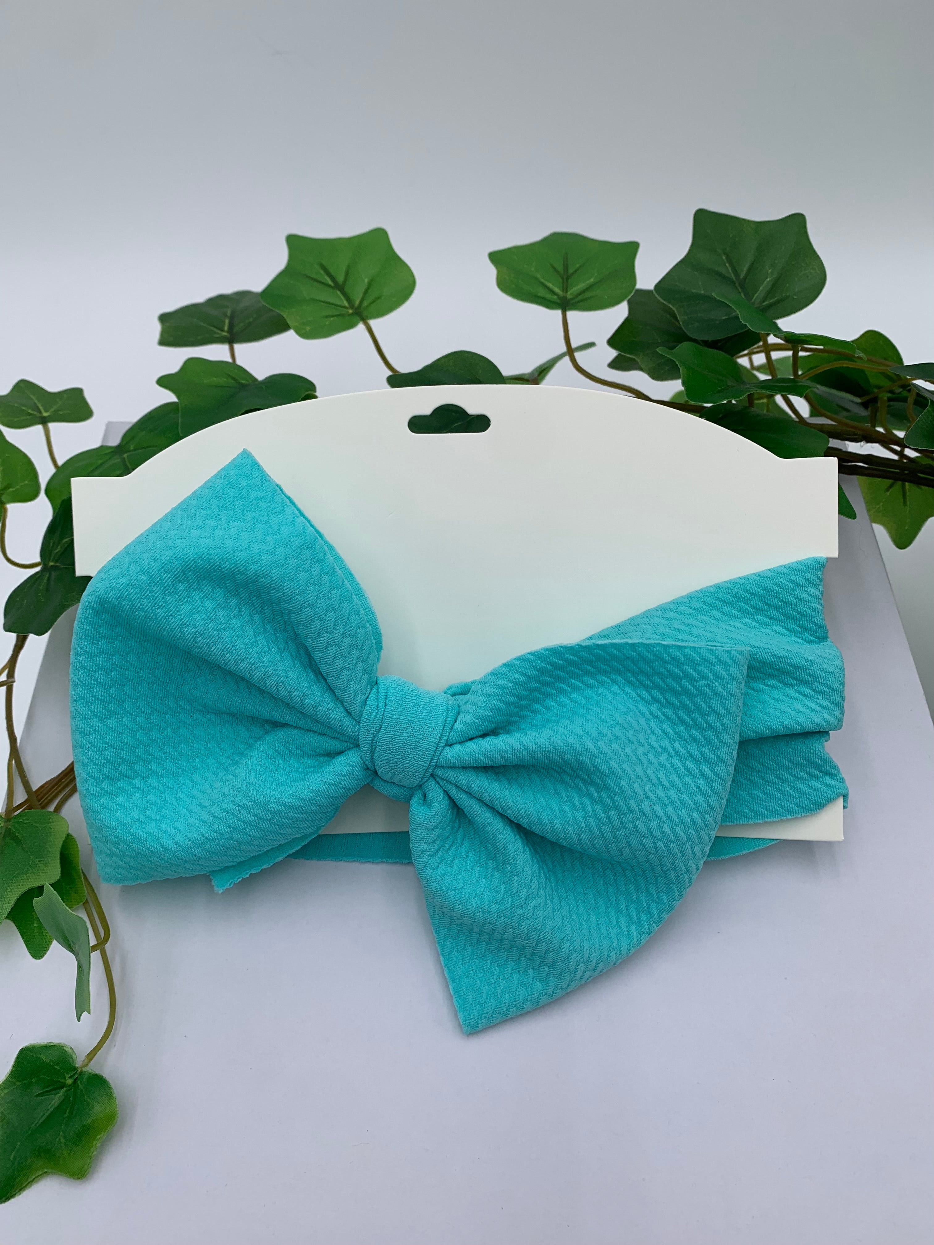 Turquoise bow tie on a white card with green leaves in the background