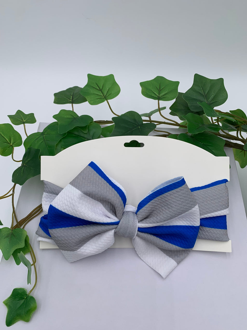 Gray, white, and blue striped bow on a white card with green leaves in the background