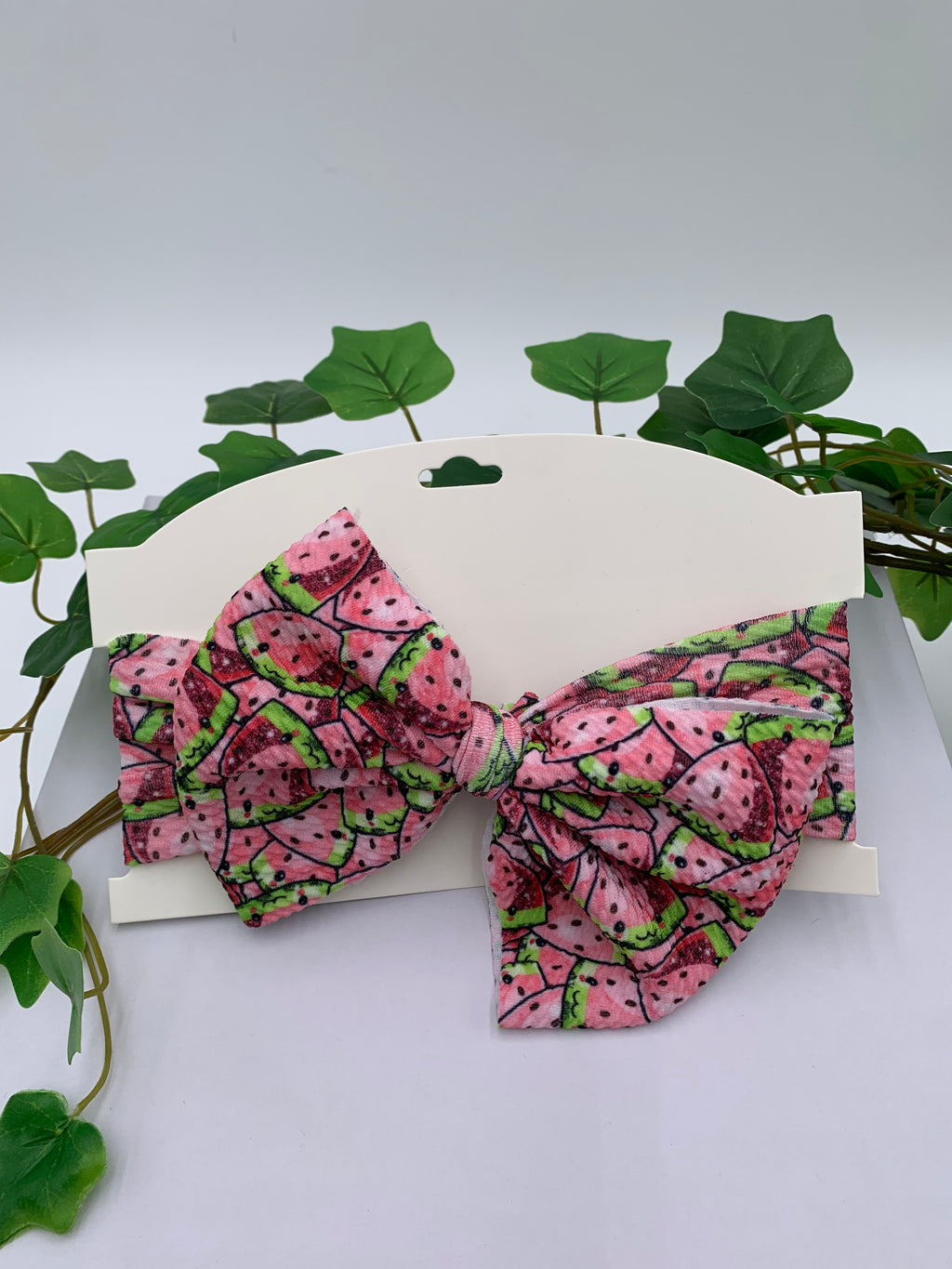 Watermelon slices themed big bow headband on a white card with a white background and greenery 