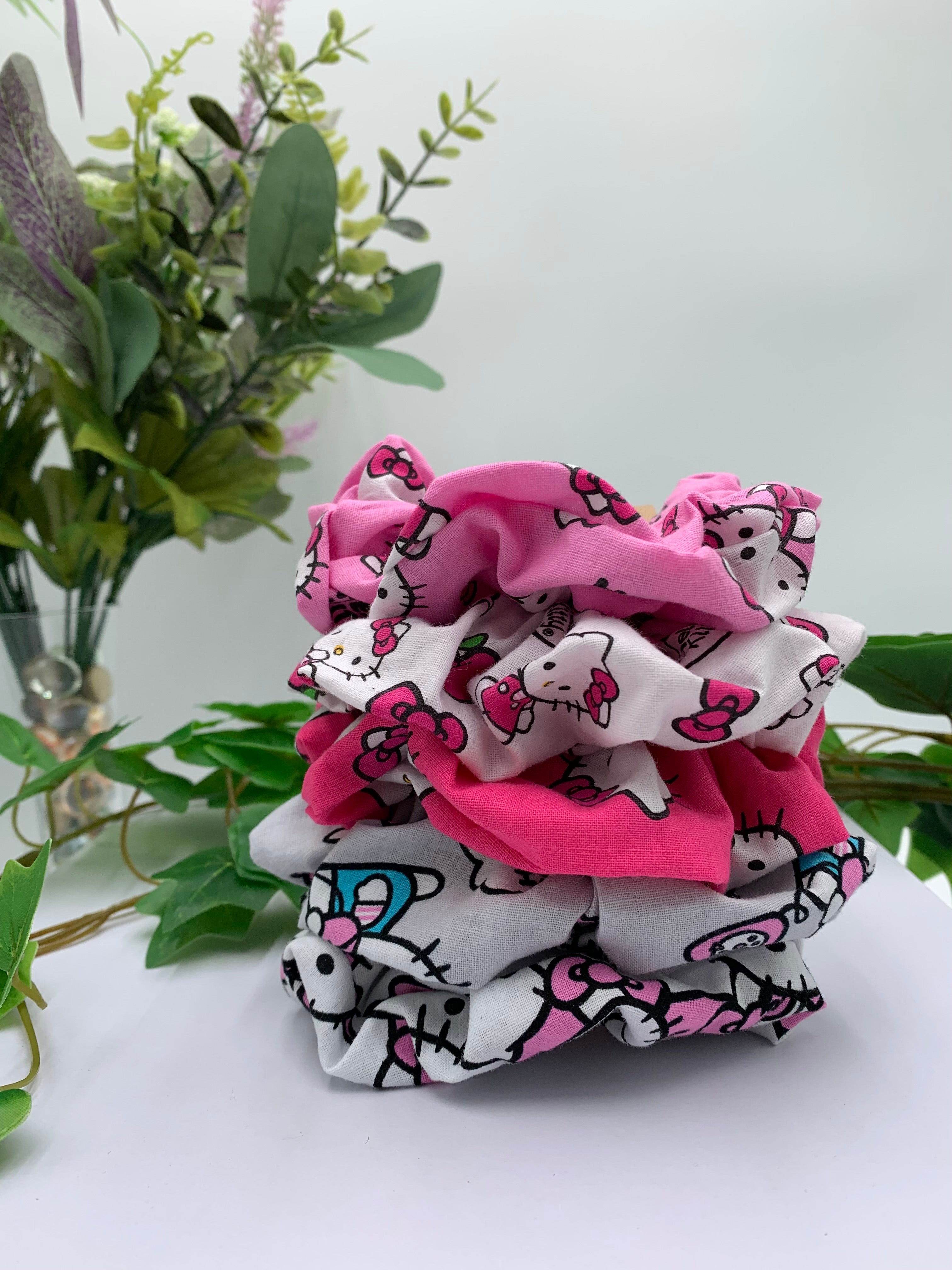 Stack of Hello Kitty-themed scrunchies on a white surface with green plants in the background