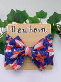 4th of July stars themed big bow headband on a wooden board with text "Newborn" with a white background and greenery  