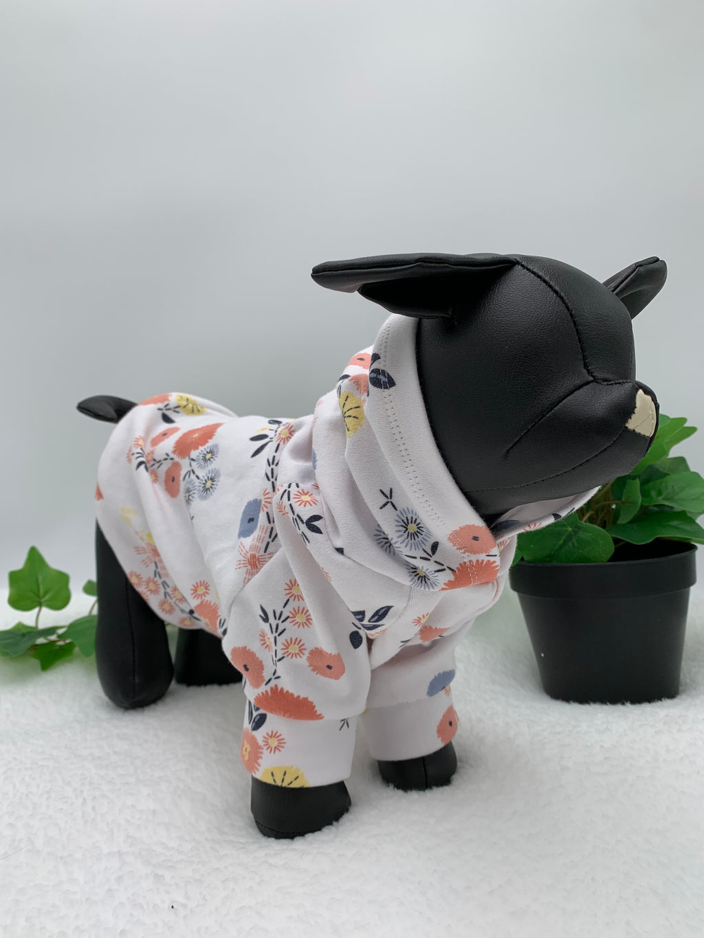 Black dog mannequin with floral pattern hoodie on a white background with a potted green plant