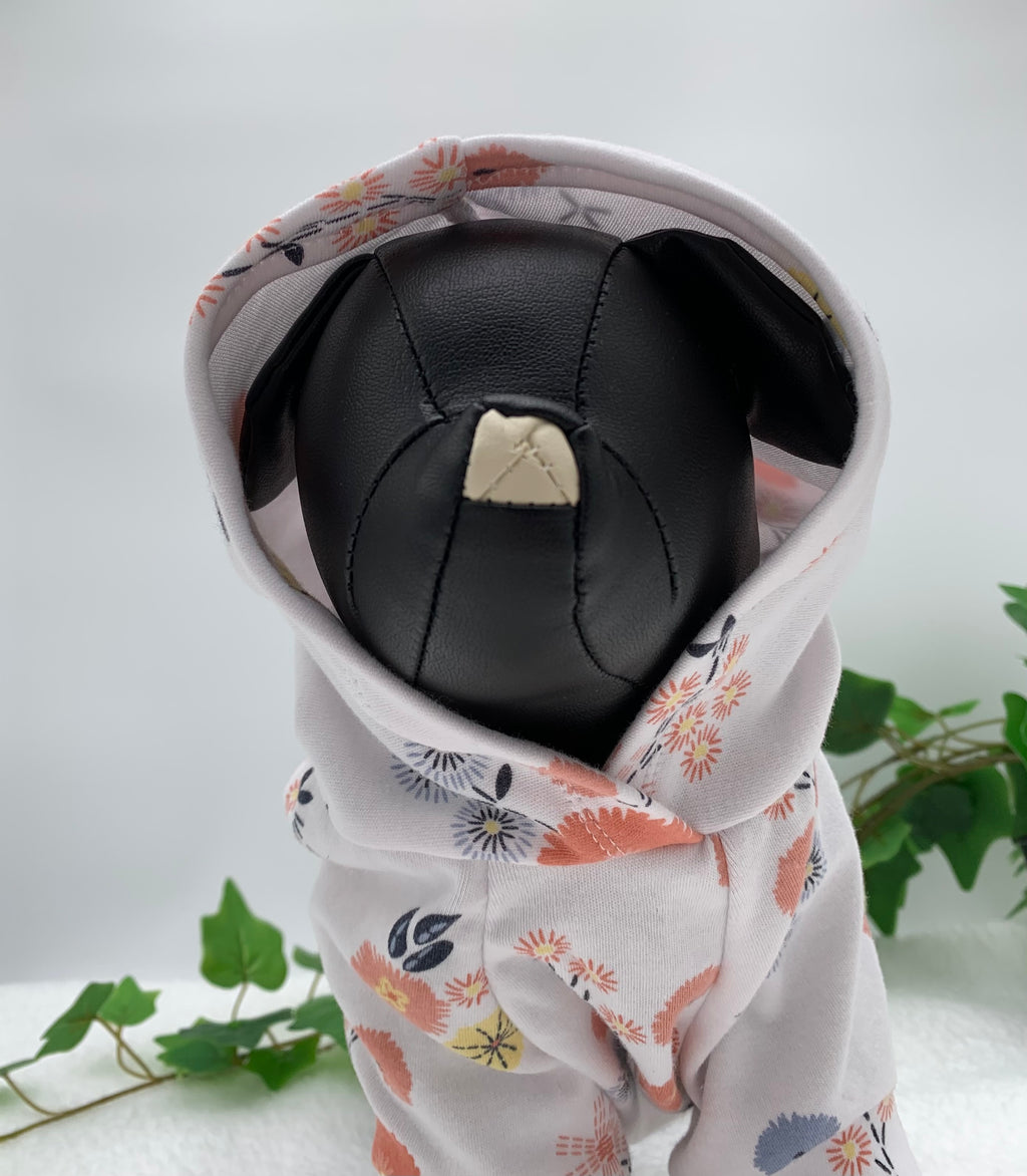 Black dog mannequin with floral pattern hoodie with hoodie up on a white background with a potted green plant