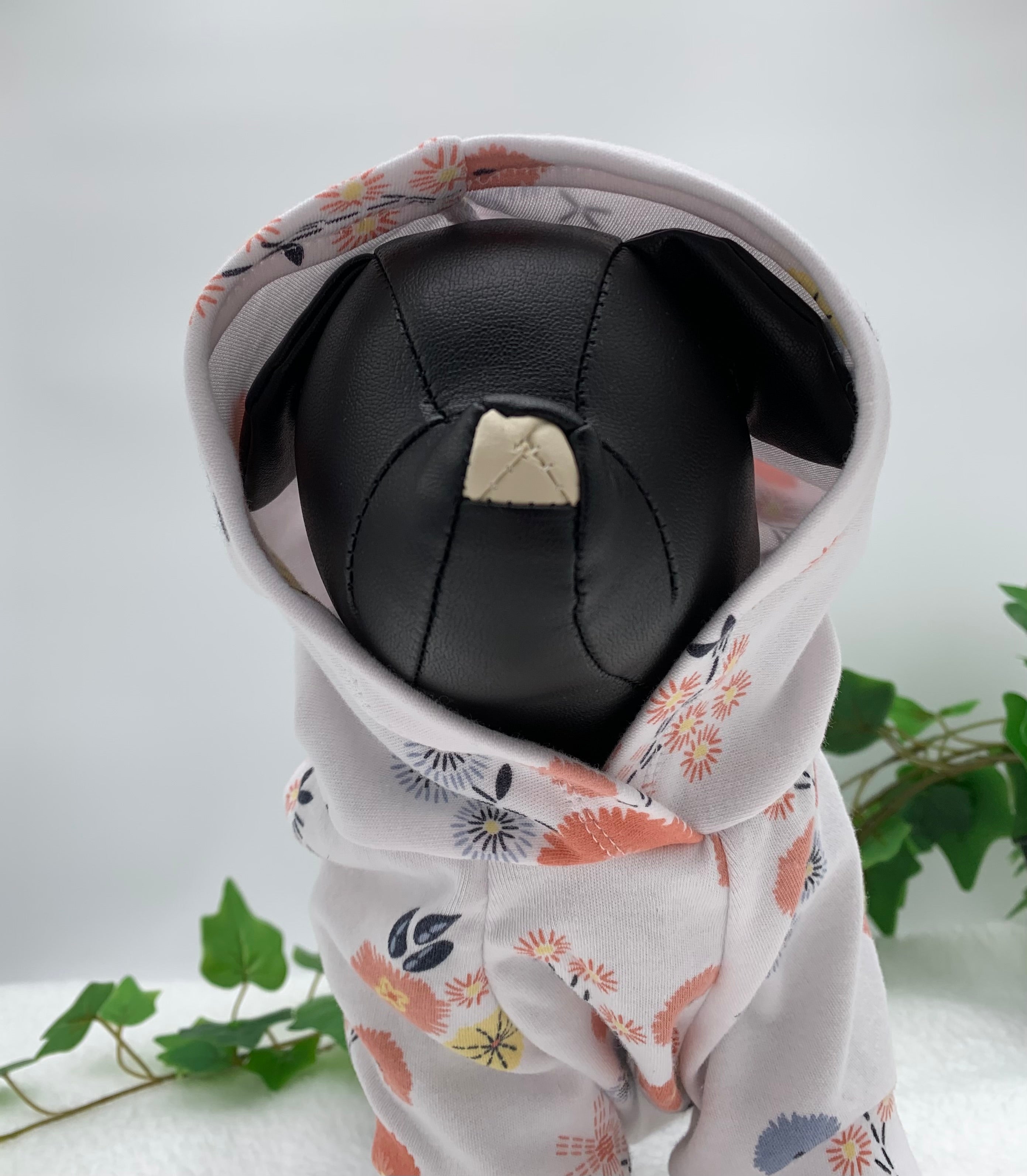 Black dog mannequin with floral pattern hoodie with hoodie up on a white background with a potted green plant