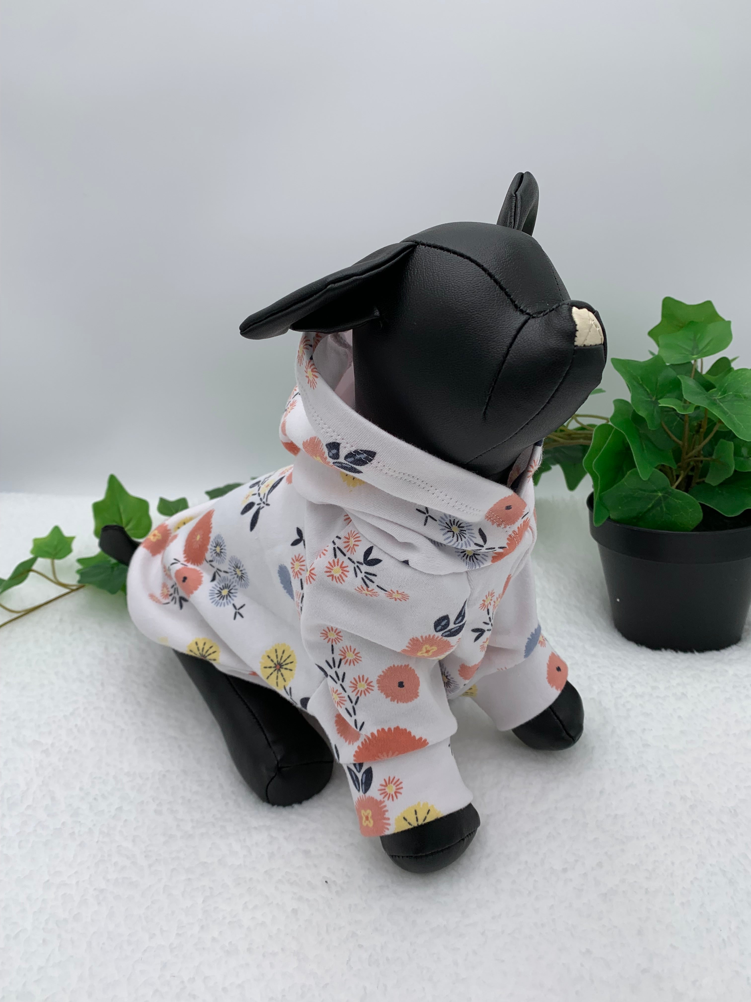 Black dog mannequin sitting with floral pattern hoodie on a white background with a potted green plant