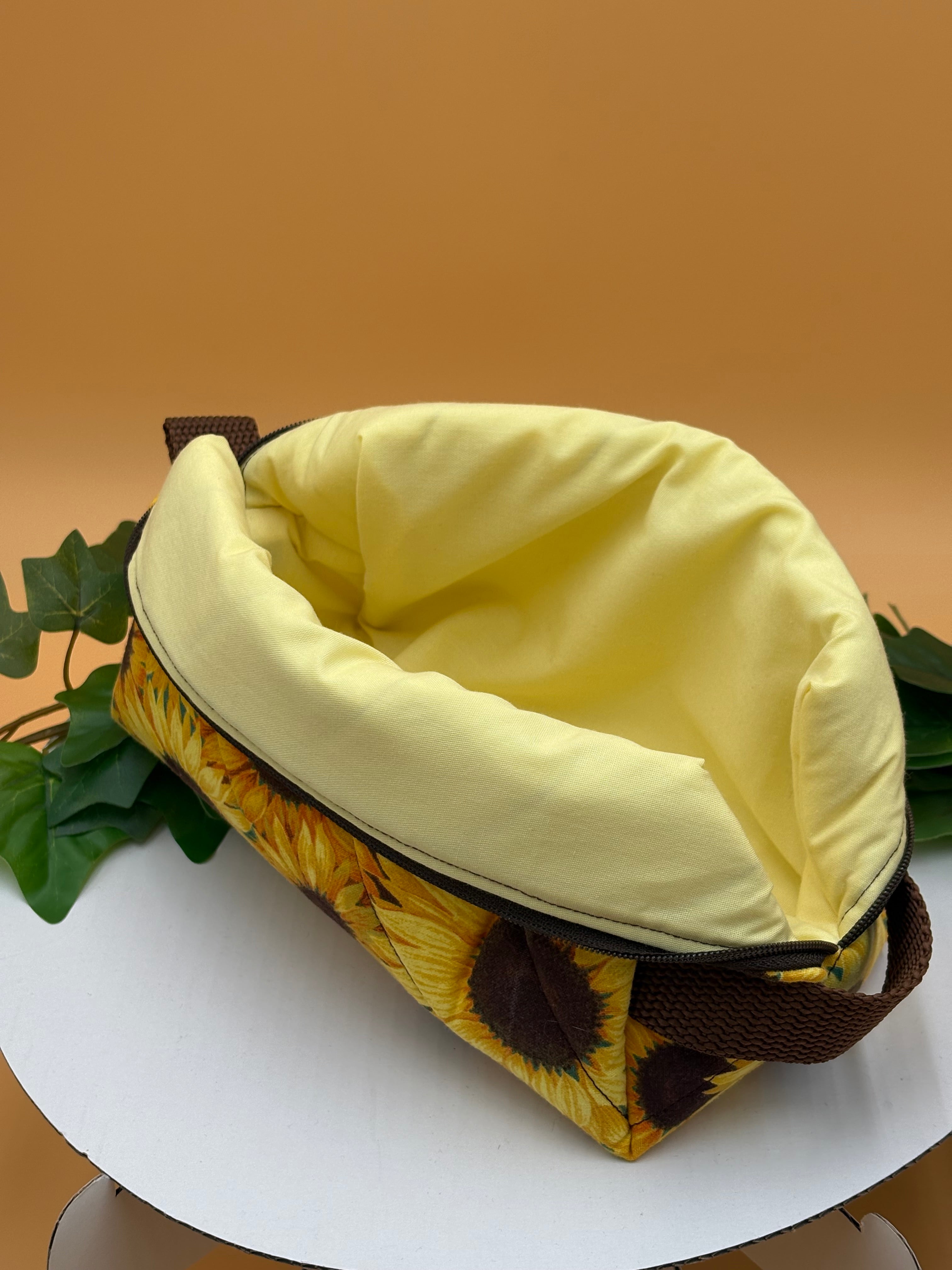 Quilted Sunflower pattern boxy makeup bag with pale yellow lining exposed on a tan background with a potted green plant