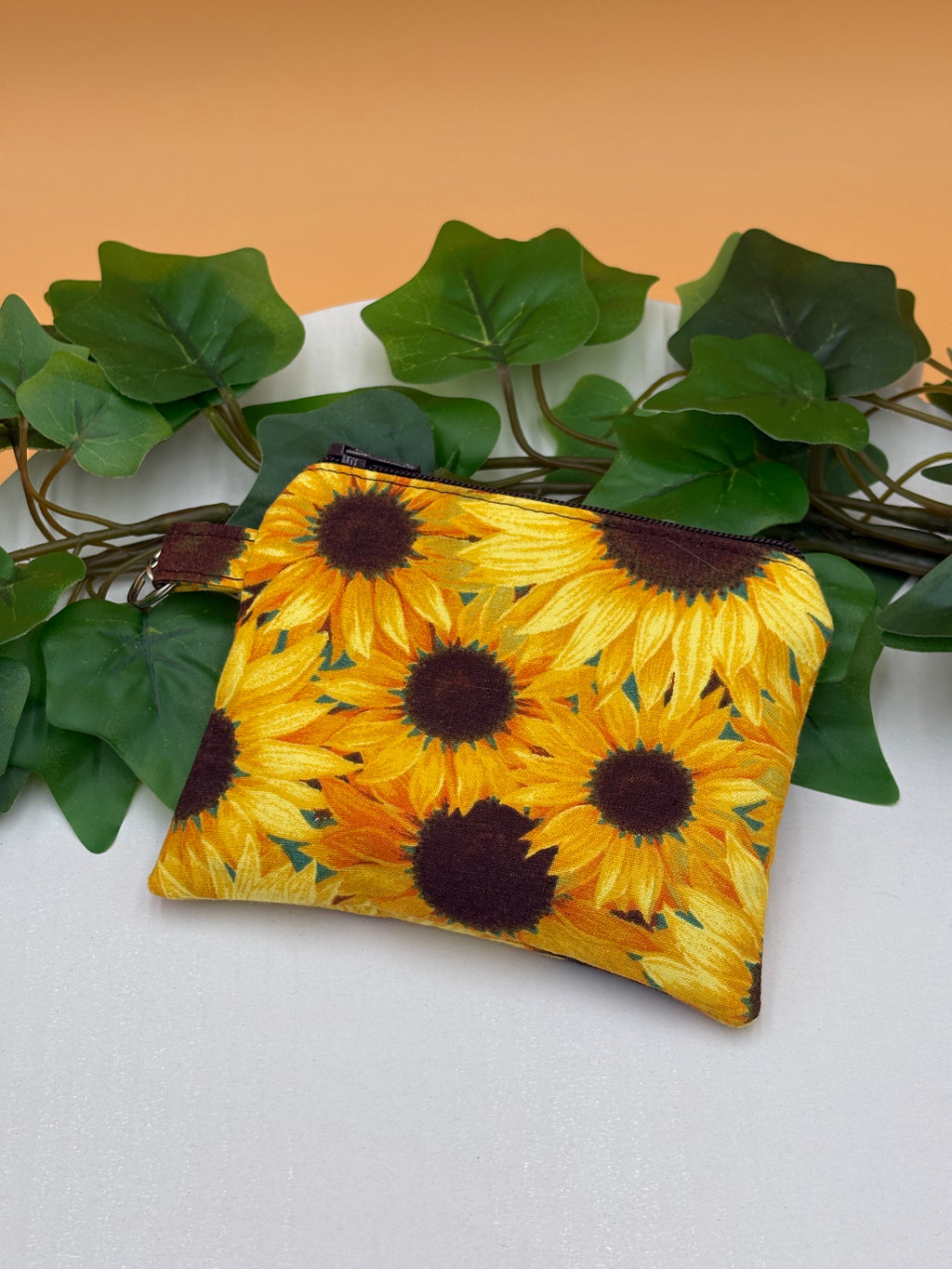 Sunflower pattern coin purse keychain on a tan background with a potted green plant